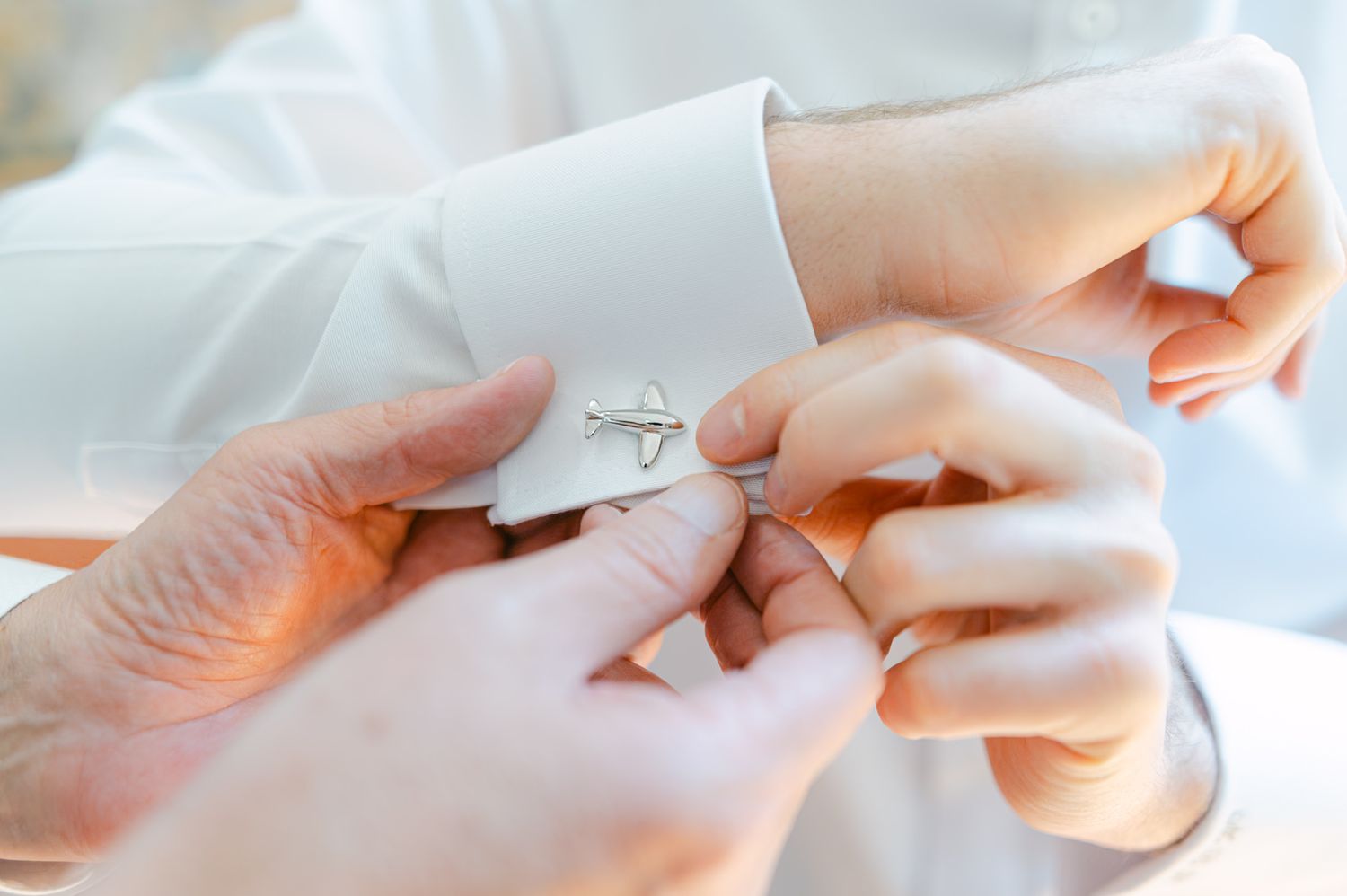 Close-up of hands fastening elegant silver cufflinks on a white dress shirt sleeve.