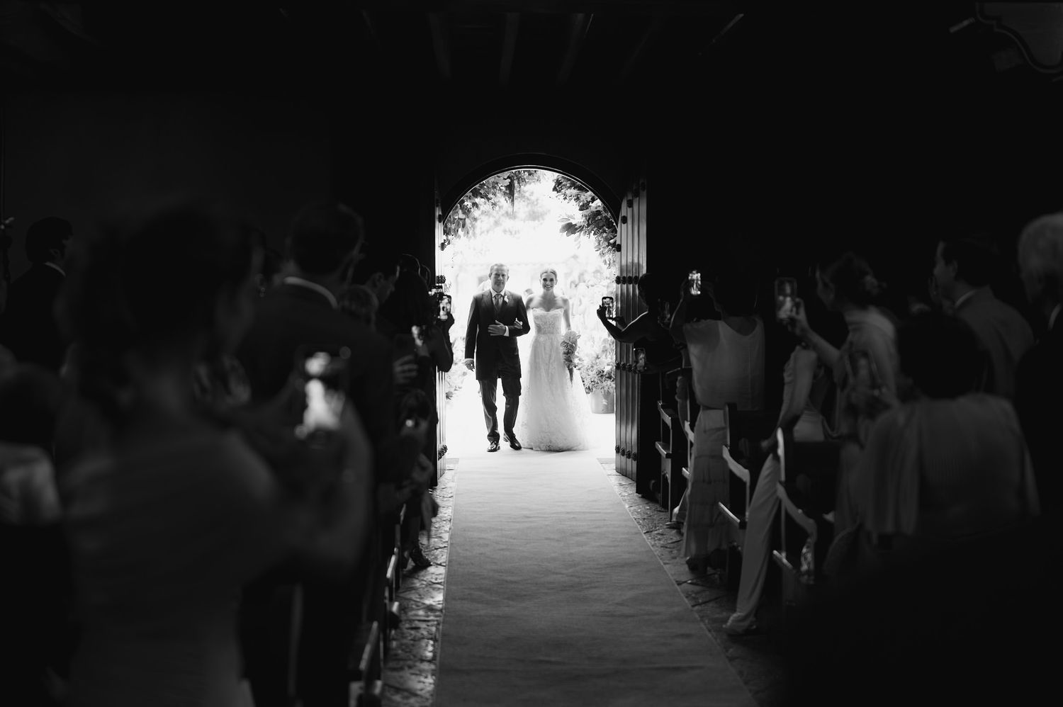 Silhouetted figures during a wedding ceremony with dramatic lighting and arched doorway.