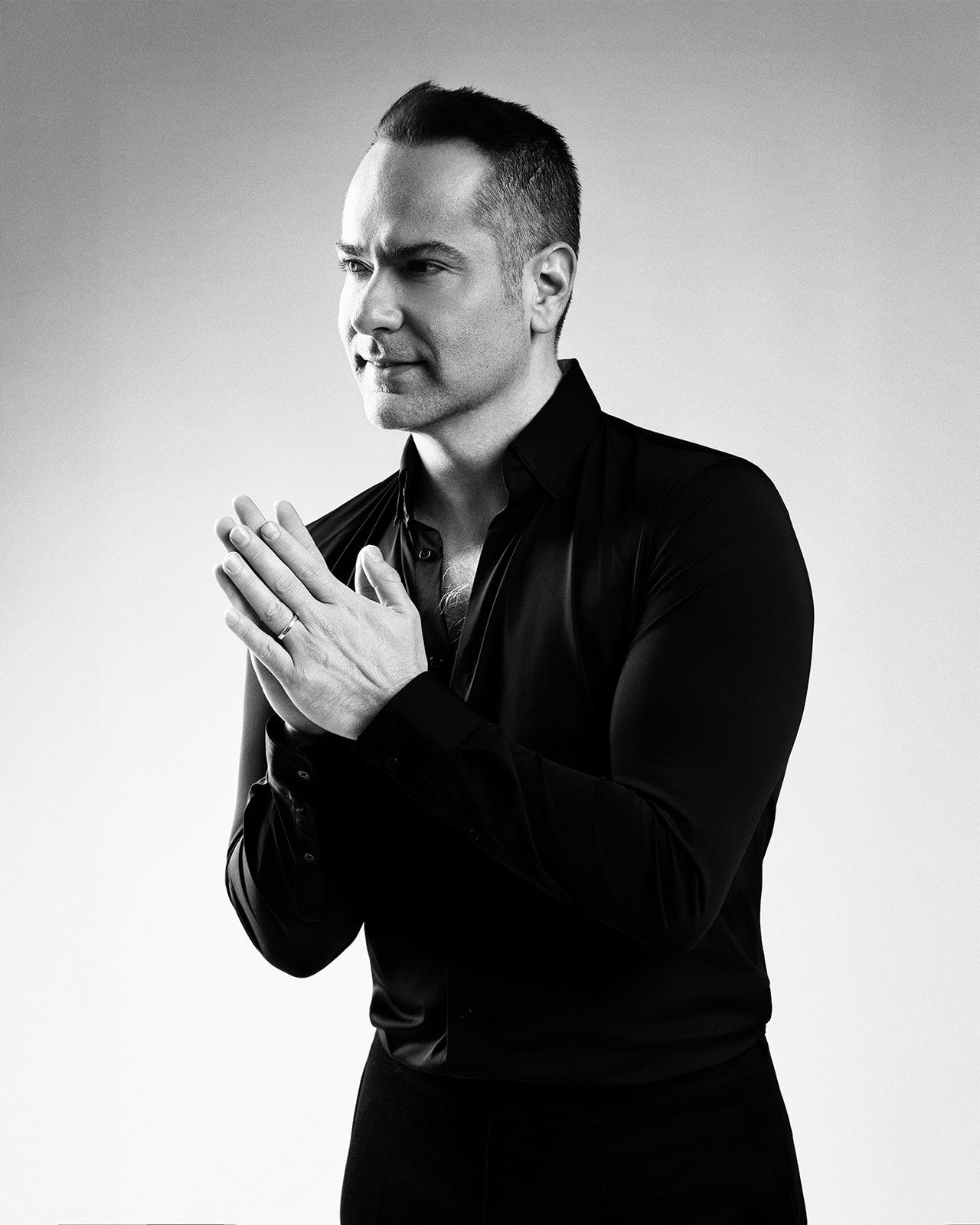 Black and white photo of a man in a black shirt with hands pressed together in a prayer pose.