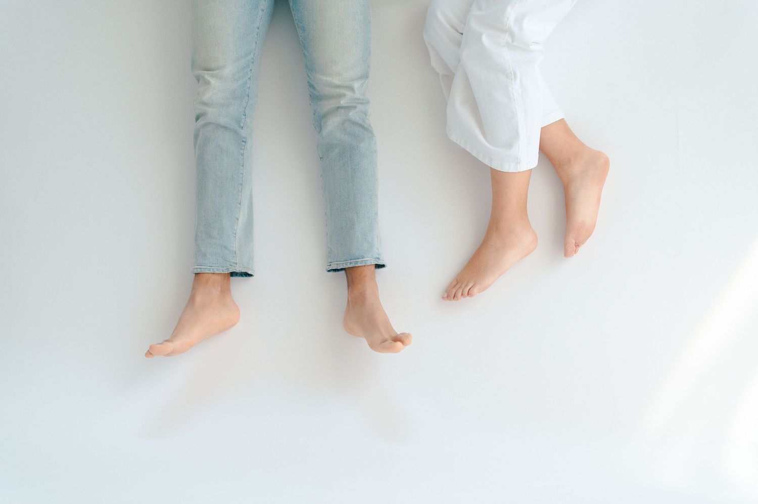 Top-down view of a couple lying on a white floor, showing their bare feet and casual denim outfits.