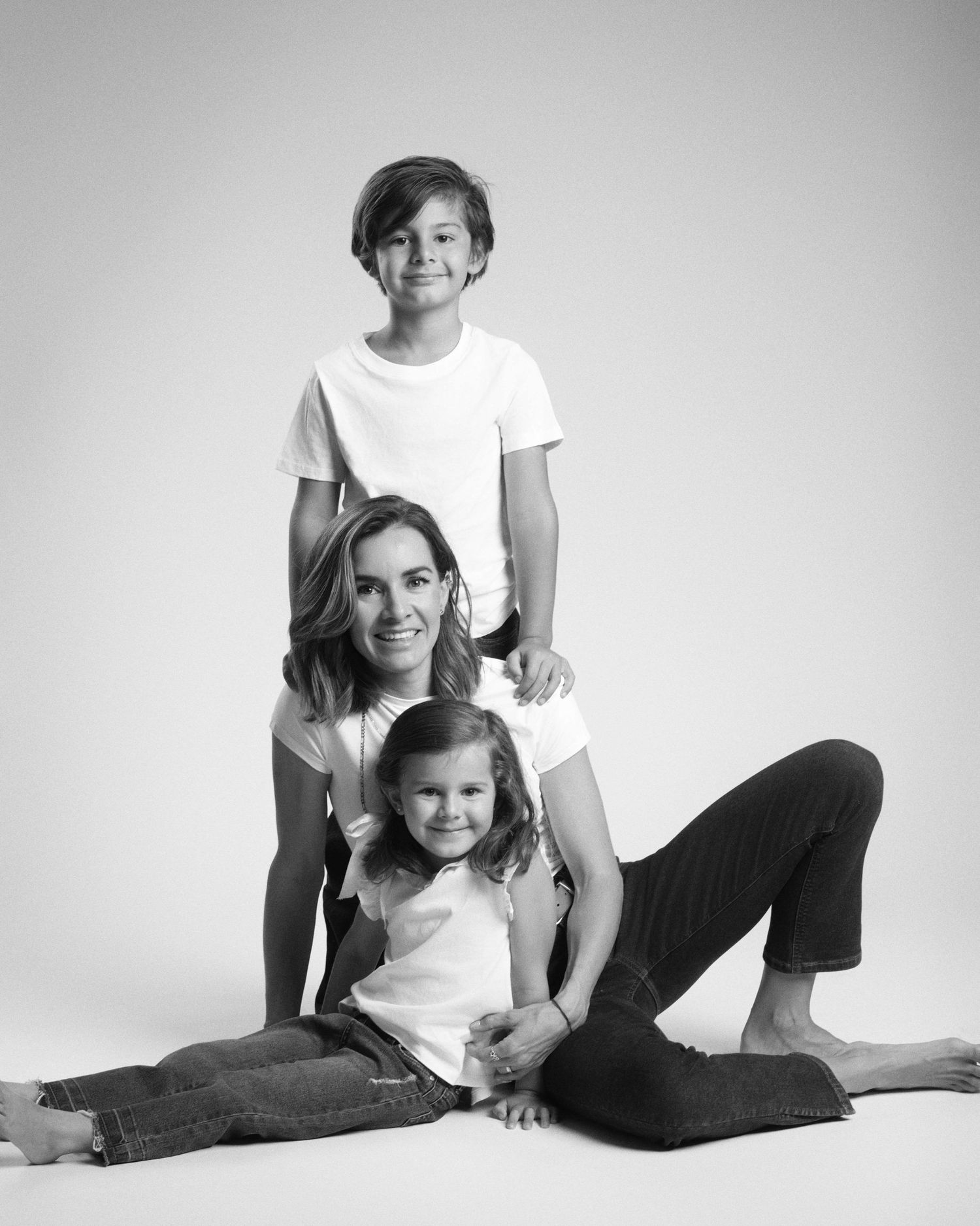 Black and white studio portrait of a mother sitting on the floor with her son and young daughter.