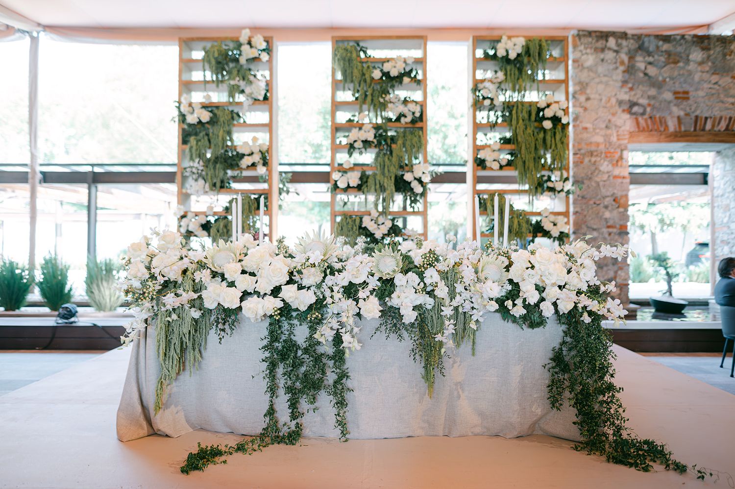 Stunning white orchid and greenery floral arrangement decorates sweetheart table at elegant wedding reception.