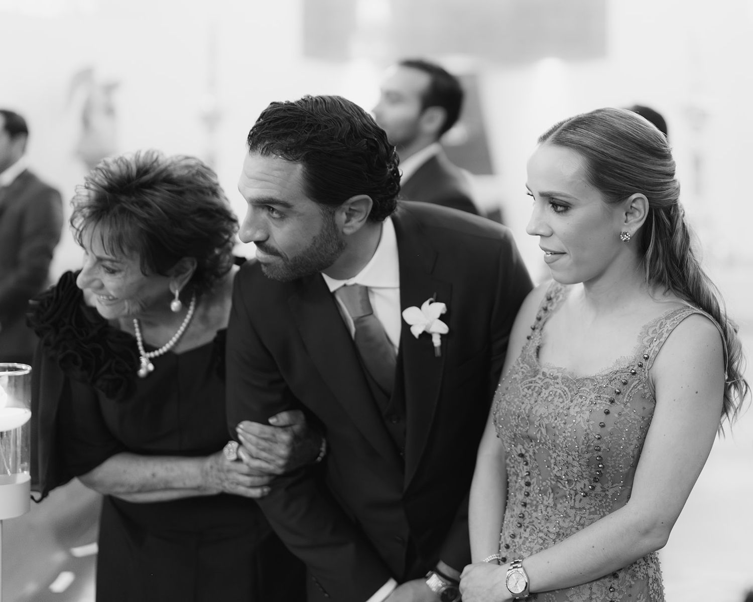 Black and white photo of groom standing between two women during wedding ceremony indoors.