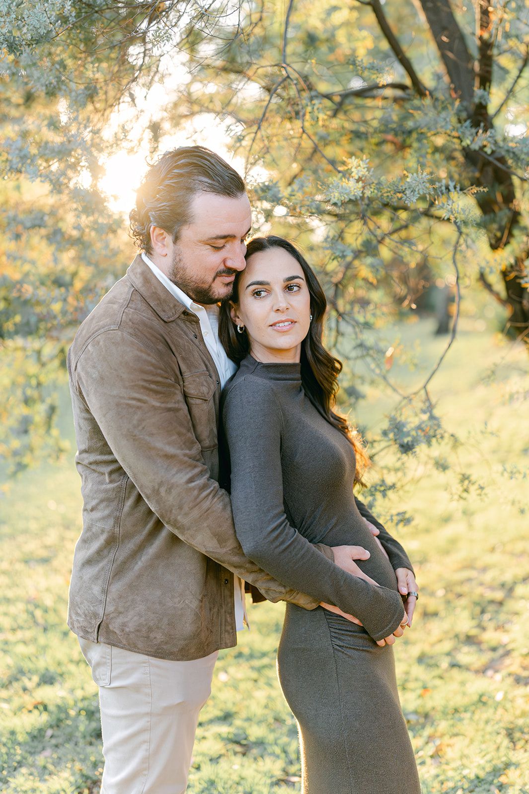 Expecting couple embracing tenderly in golden sunset light among autumn trees during maternity photoshoot.