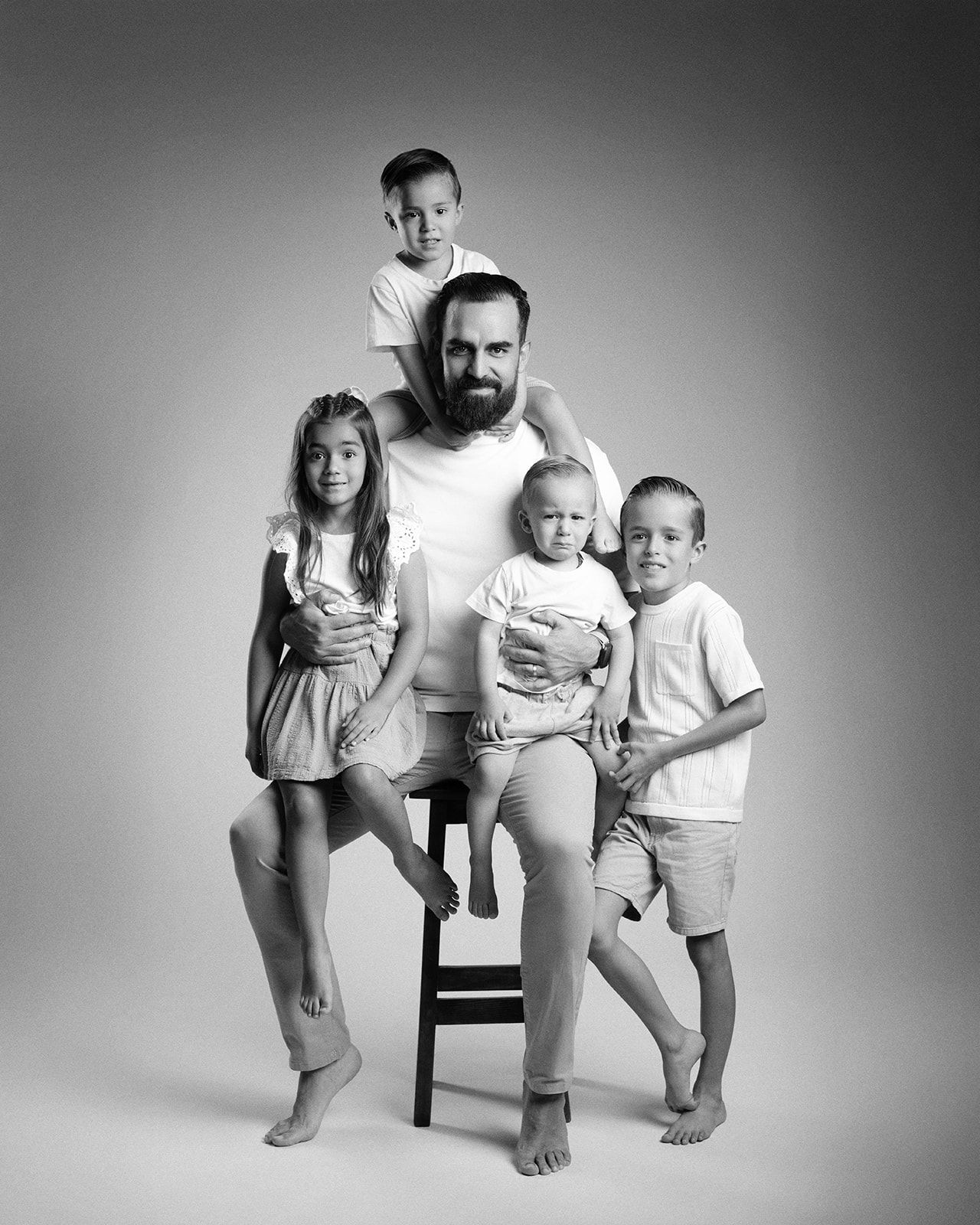 Black and white studio portrait of a bearded father seated with four young children around him.