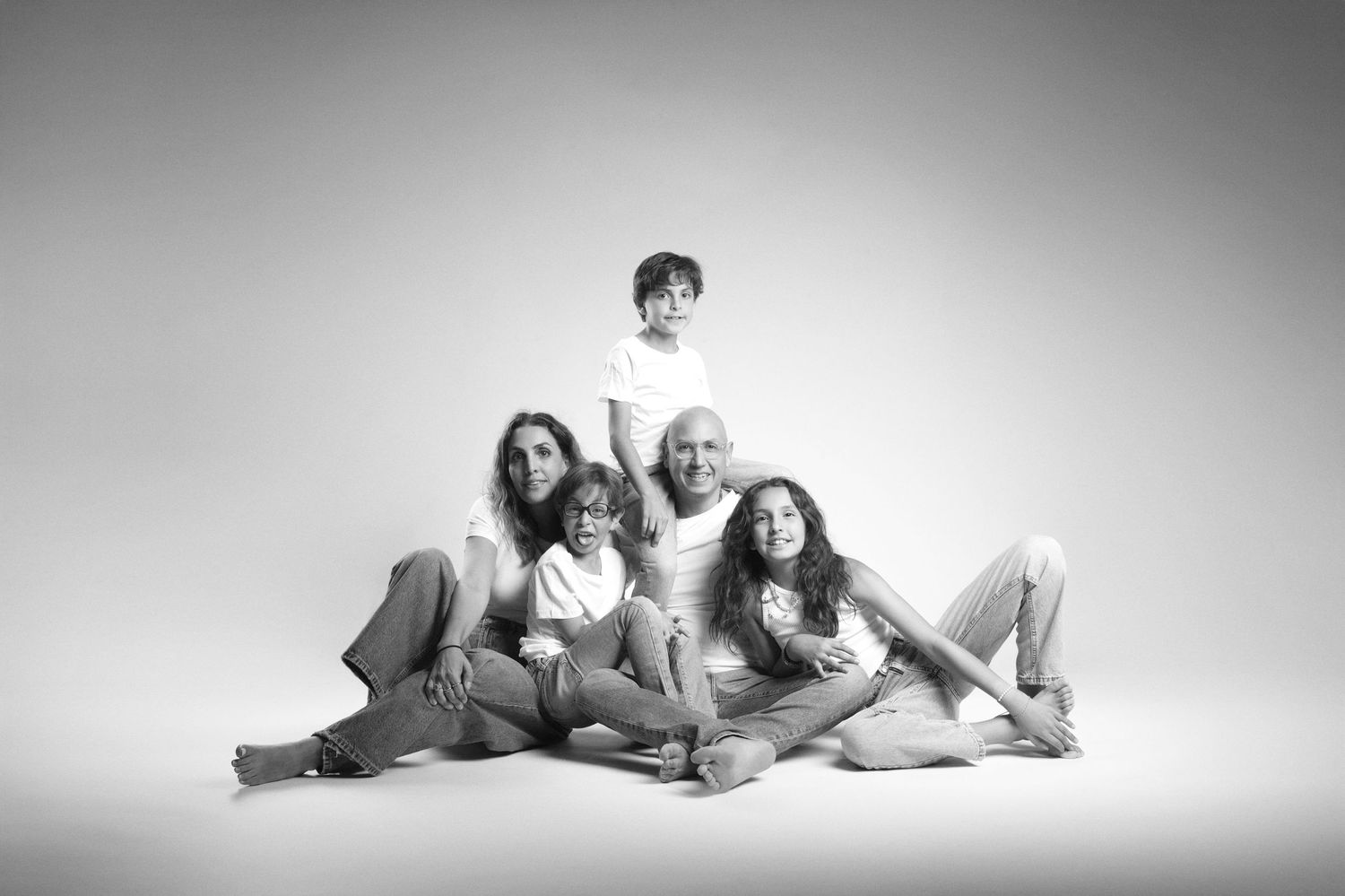 Black and white family portrait of five people sitting together on the floor in a bright studio.