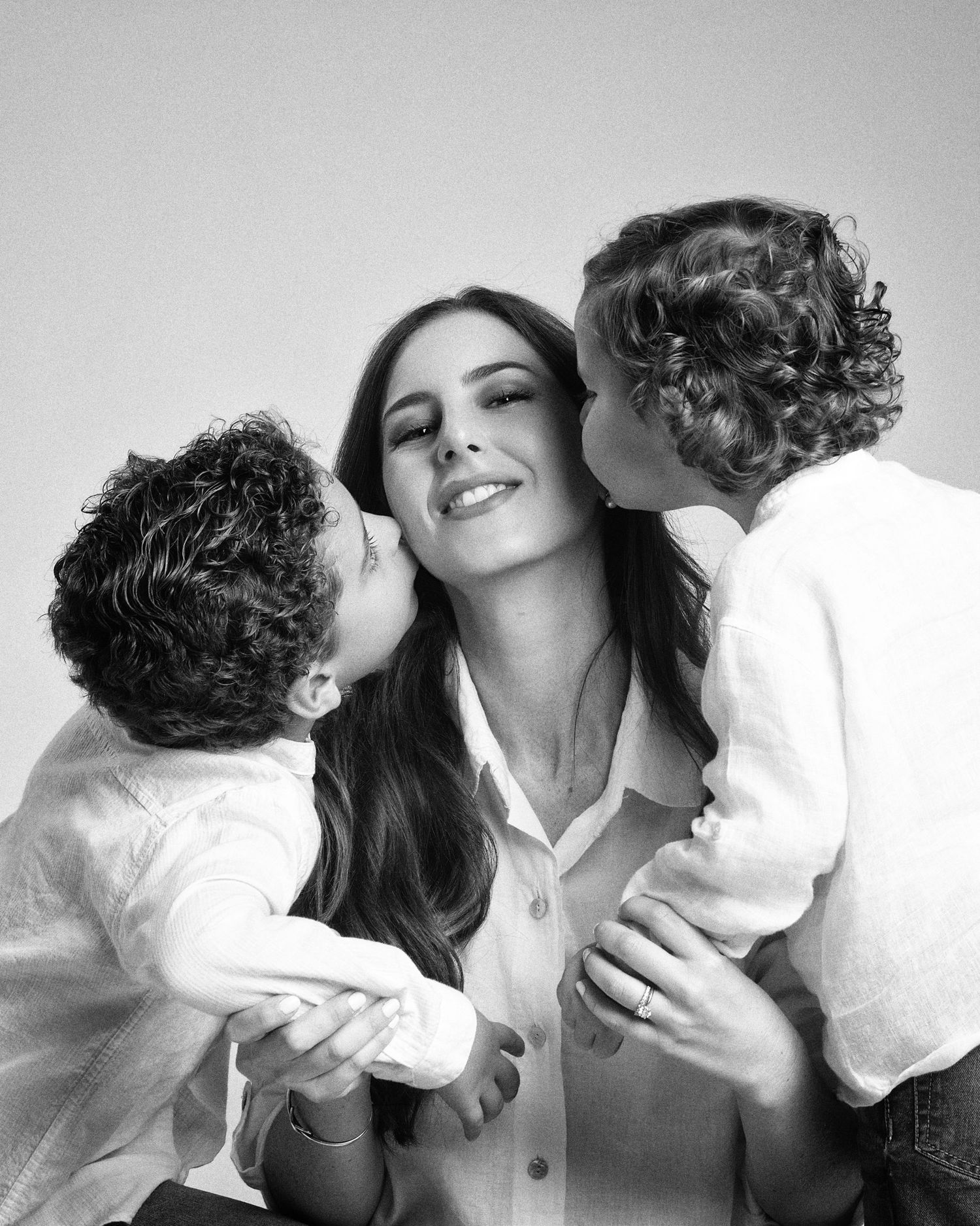 Black and white photo of a mother being kissed on cheeks by her two curly-haired children.