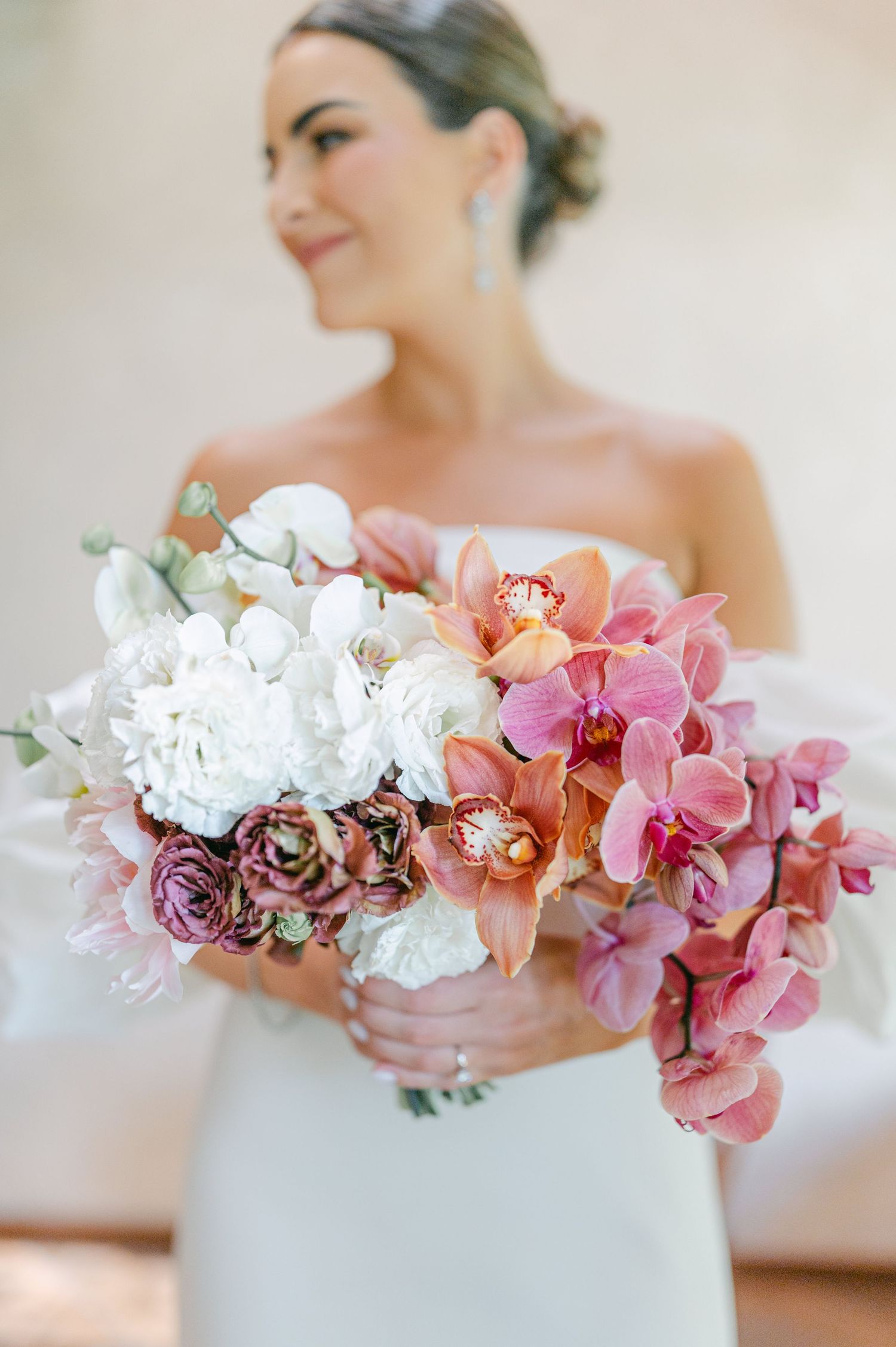 Close-up of bridal bouquet featuring pink orchids, white peonies, and dusty rose ranunculus held by bride.