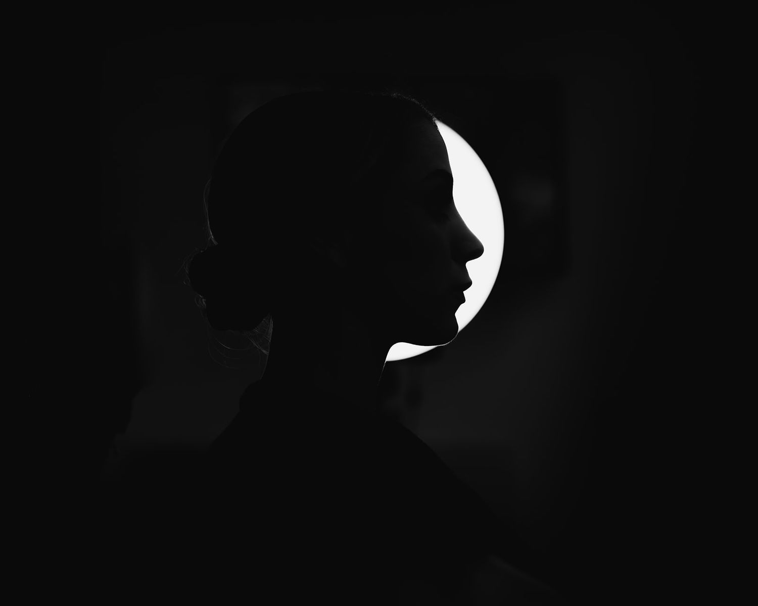 Dramatic silhouette of a woman's profile against a circular backlit background in black and white.