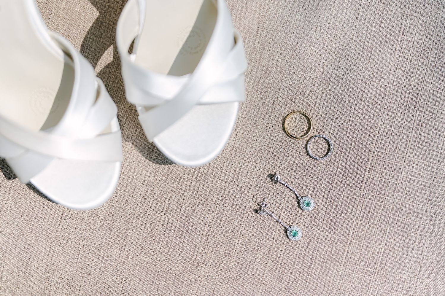 Bridal accessories flat lay featuring white strappy heels, gold wedding bands, and turquoise drop earrings.