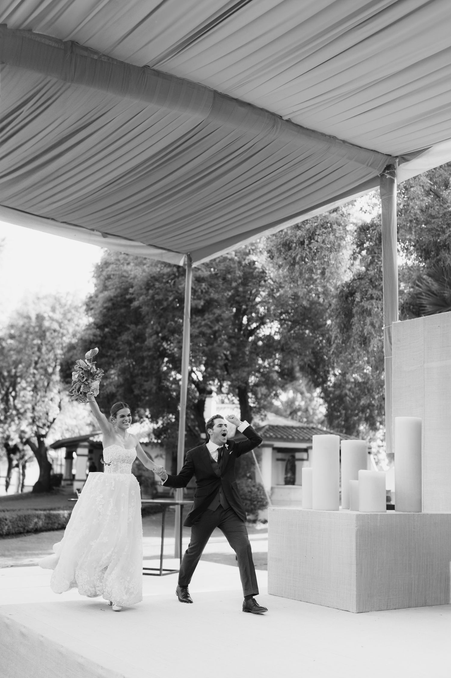 A couple dances energetically under a white tent canopy during an outdoor wedding celebration.
