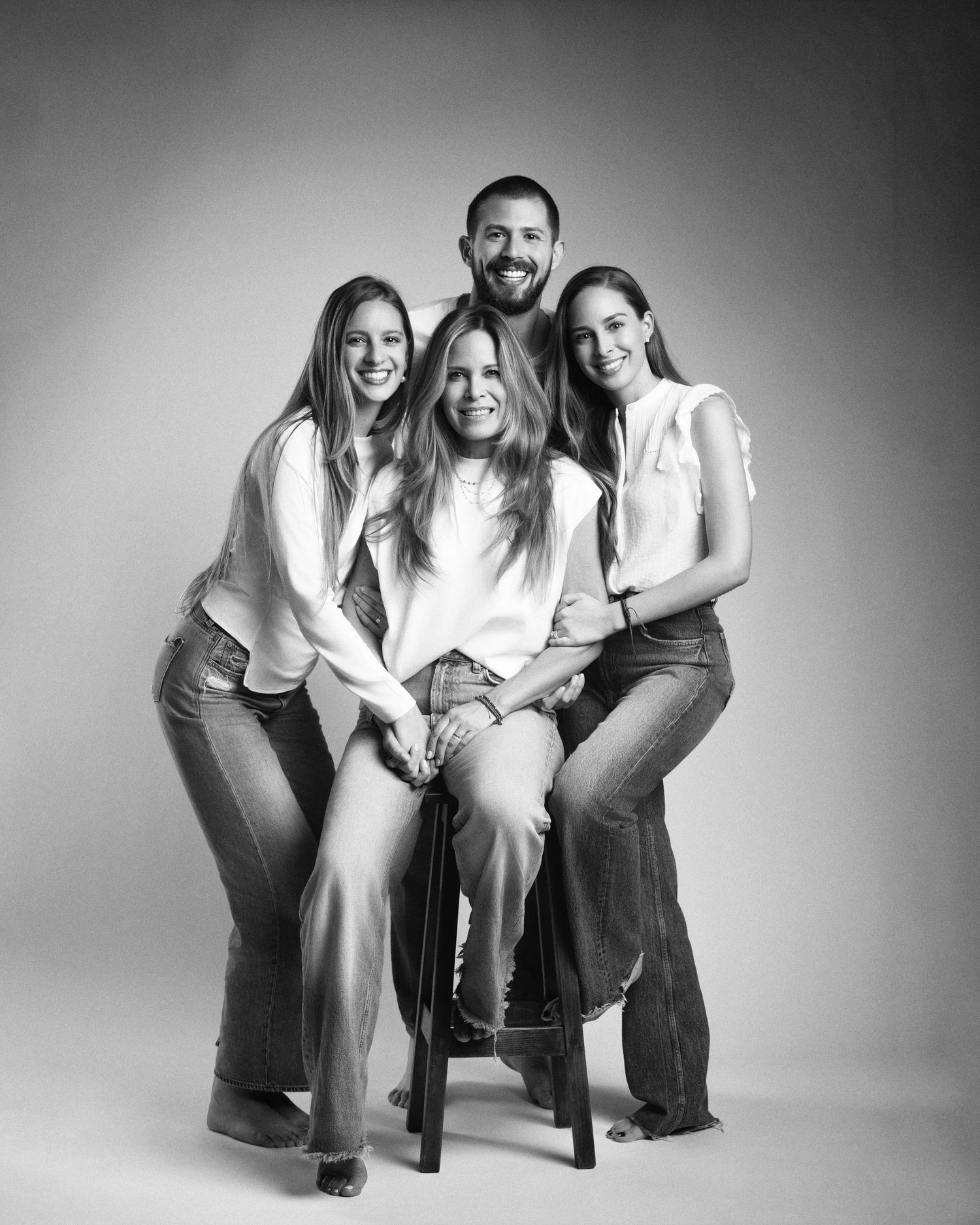 Black and white family portrait of four people posing together in jeans and white tops in a studio.