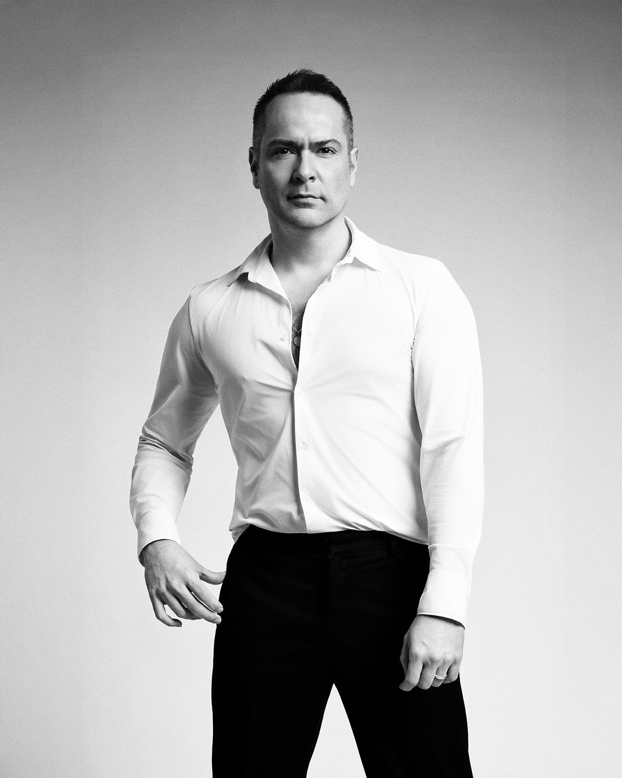Black and white portrait of a muscular man in a white button-up shirt posing confidently.