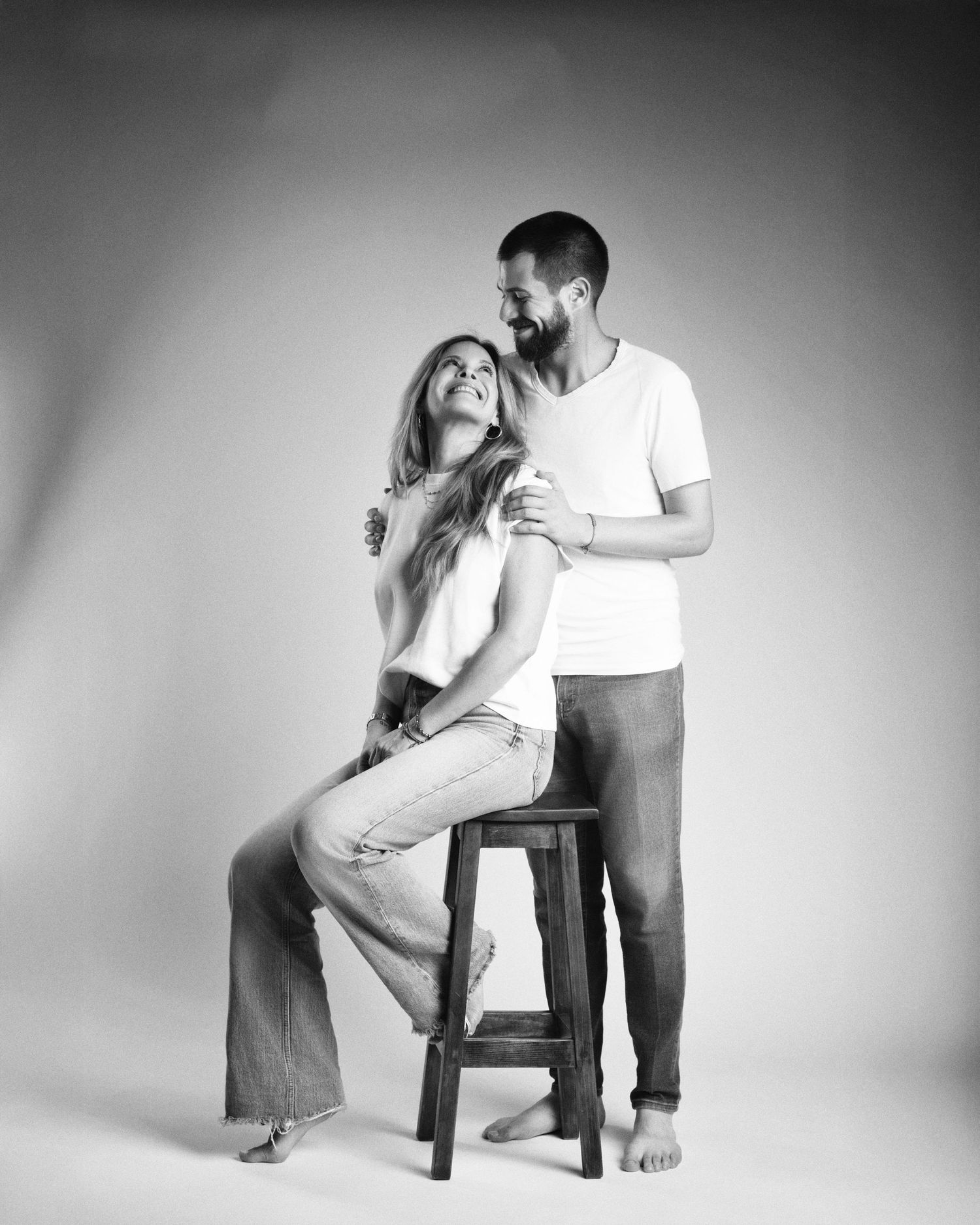 Black and white studio portrait of a couple, woman seated on a stool with man standing behind her.
