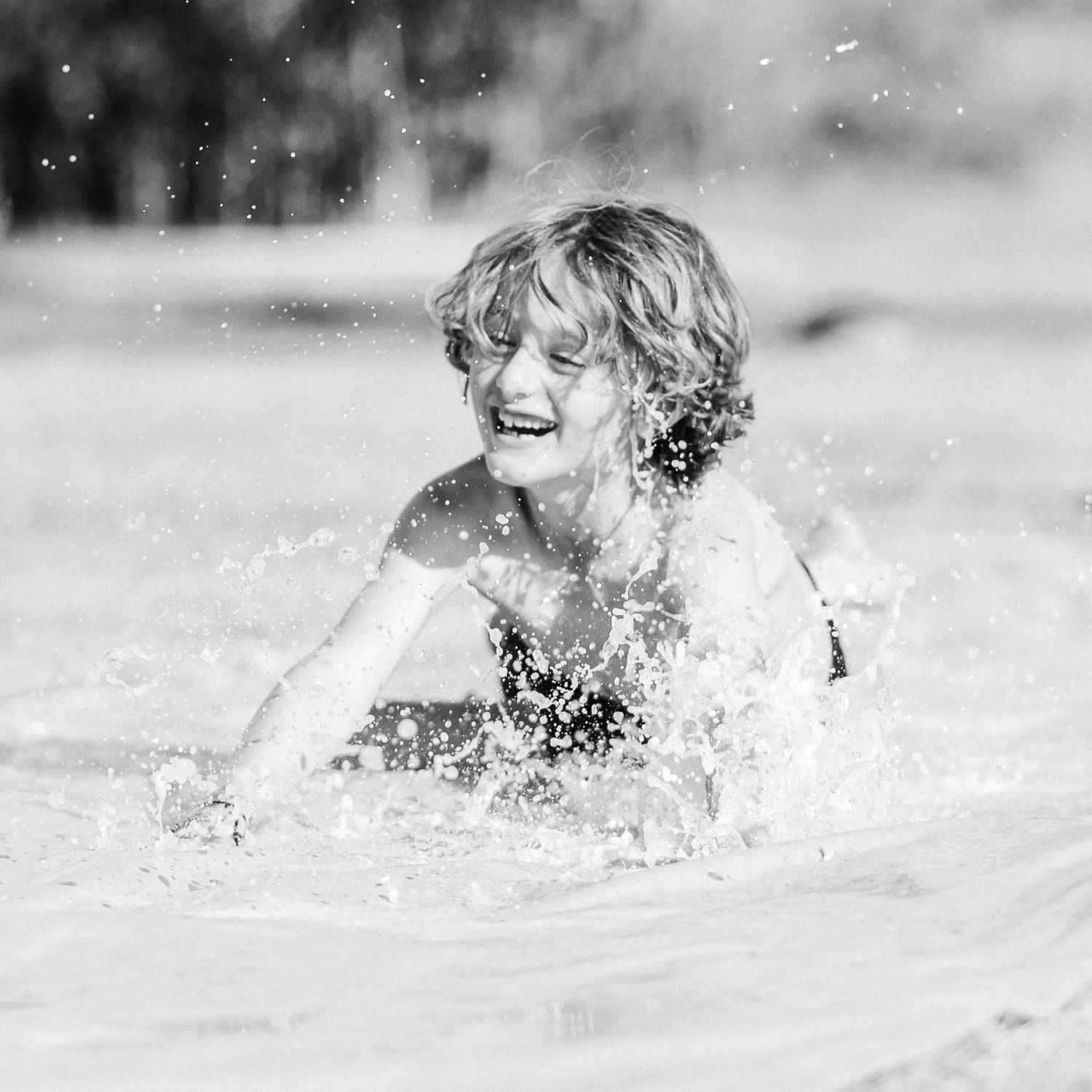 Black and white photo of a child laughing and splashing in ocean waves.