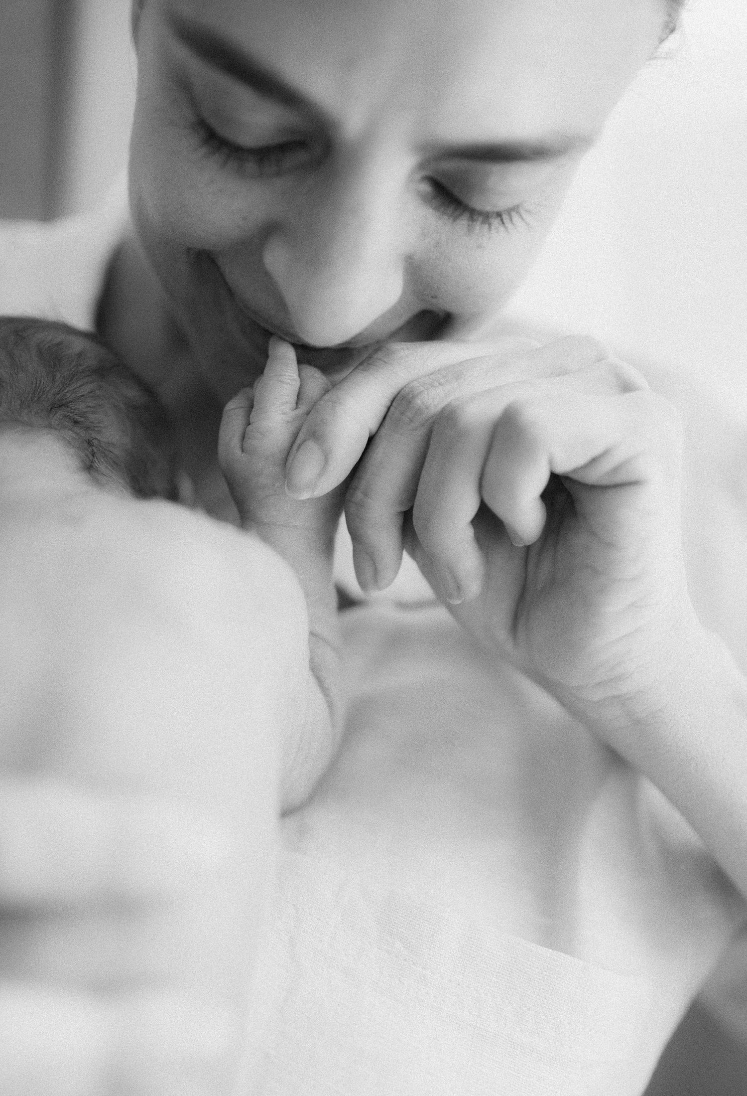 Black and white photo of a mother tenderly kissing her newborn baby's tiny hand.