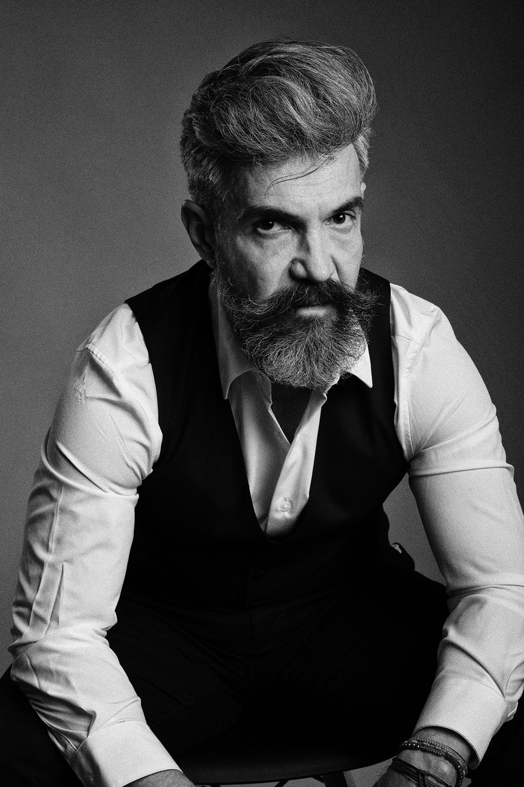 Black and white portrait of a distinguished bearded man in a white shirt and black vest, seated.