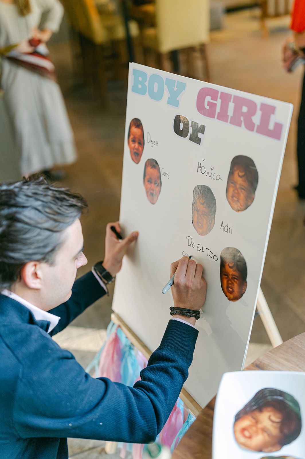 Man writing names on boy or girl gender reveal poster board at baby shower event.