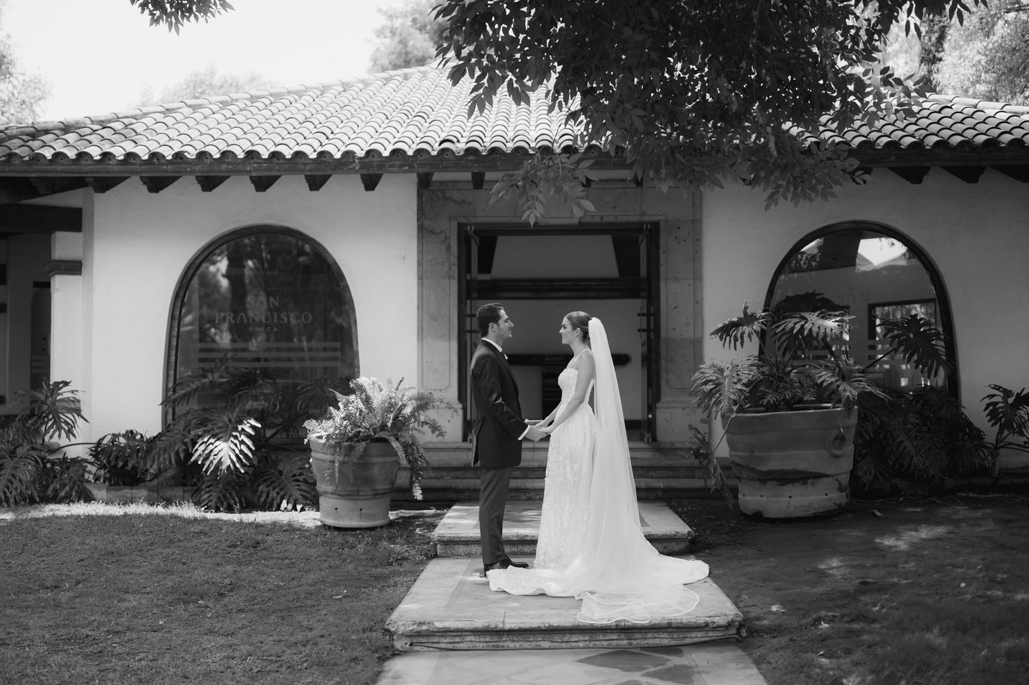 Black and white photo of bride and groom standing together outside a Spanish-style wedding venue.