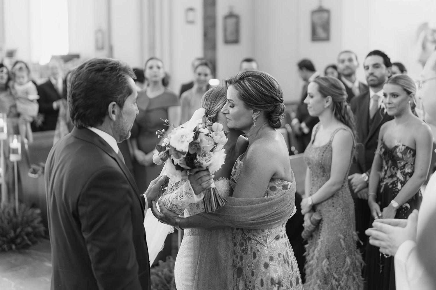 Black and white photo of bride embracing a guest while holding her bouquet at wedding ceremony.