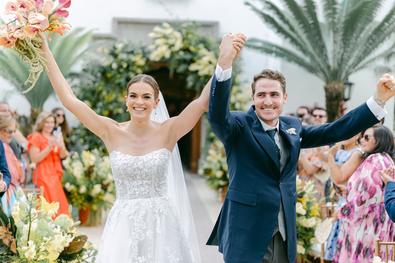 Beautiful outdoor wedding celebration with palm trees and floral decorations in background.