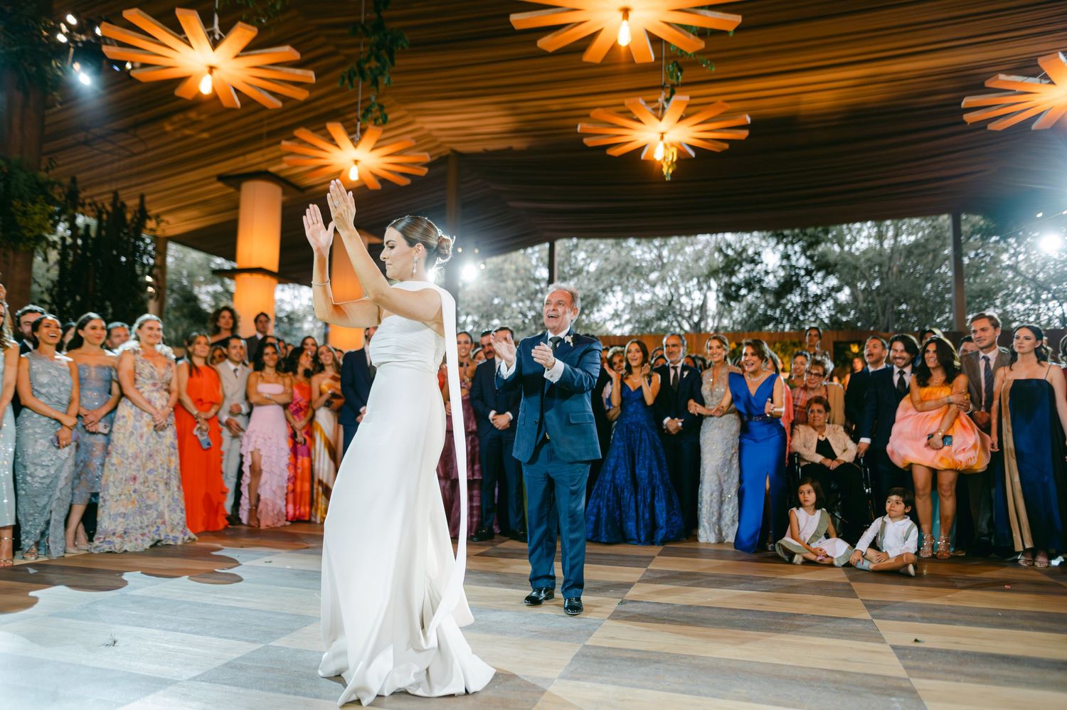 Bride in white gown and groom in blue suit dance together at elegant wedding reception.