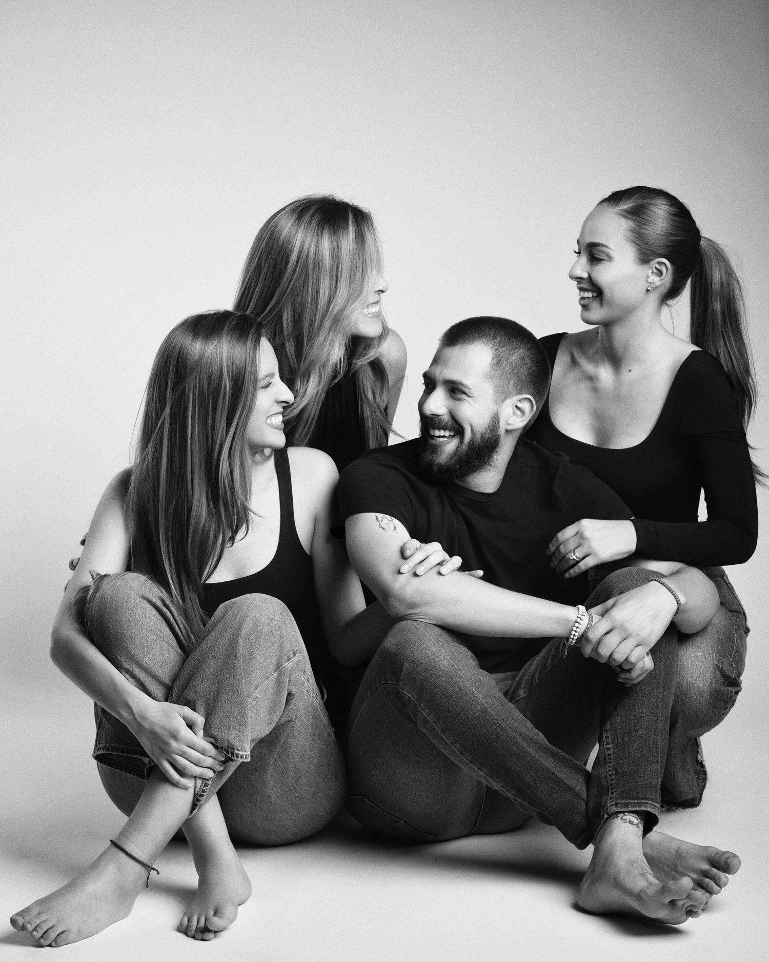 Black and white studio photo of four family members sitting on the floor together, laughing and smiling.
