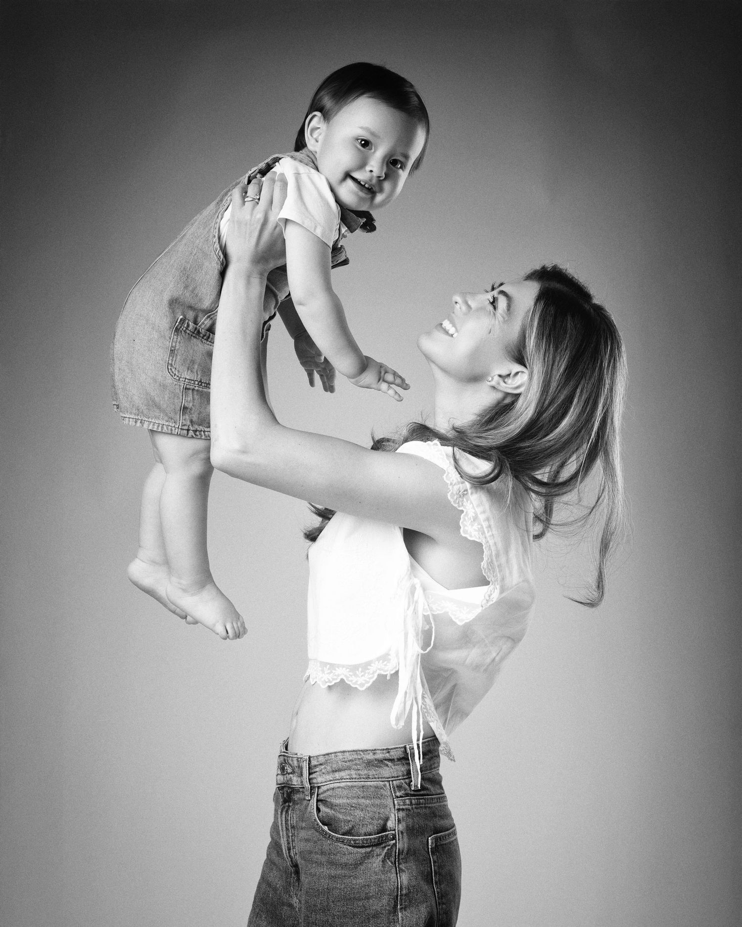 Black and white photo of a mother lifting her laughing young daughter in the air.