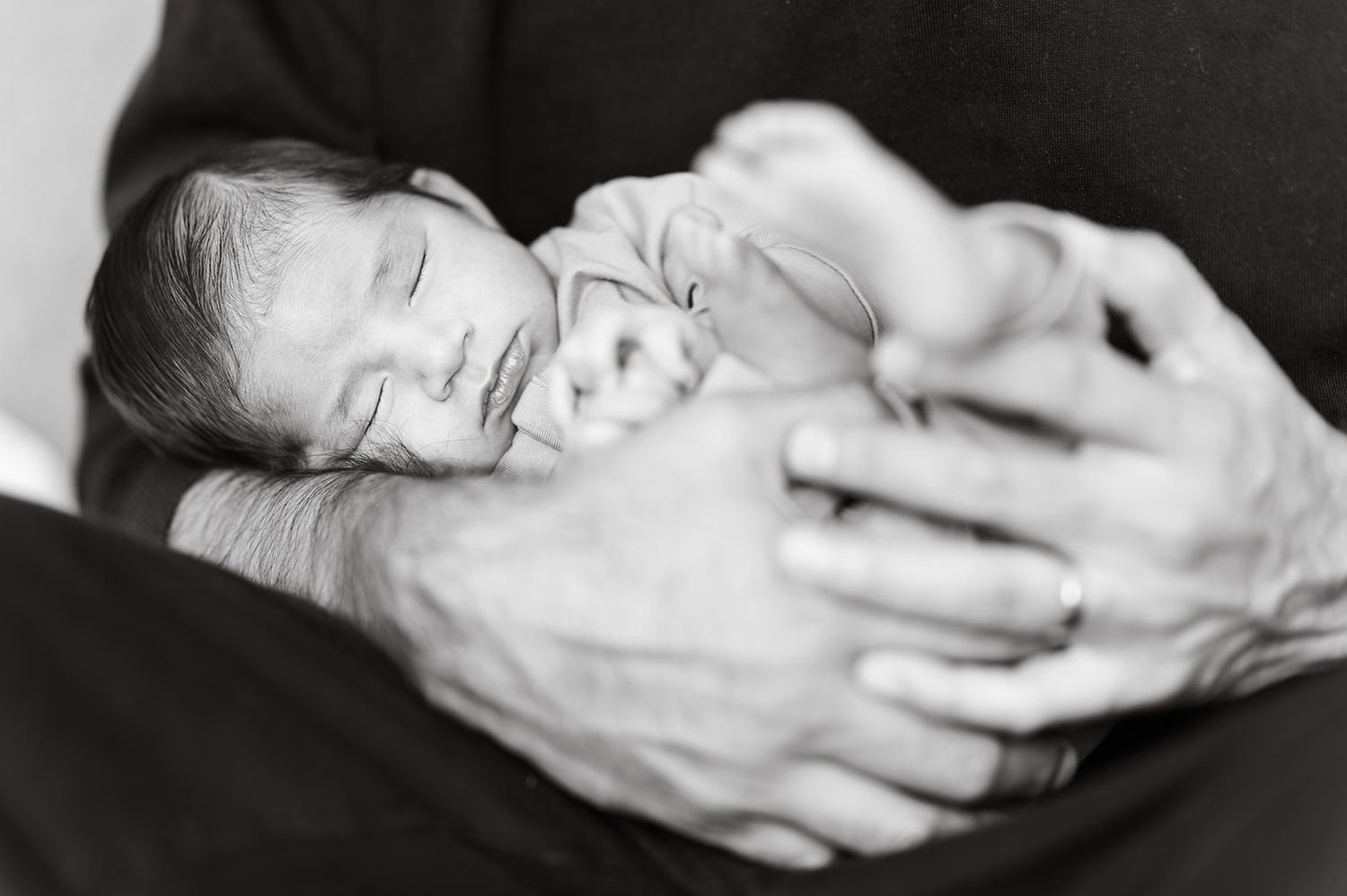 Black and white newborn portrait of a sleeping baby cradled gently in an adults hands.