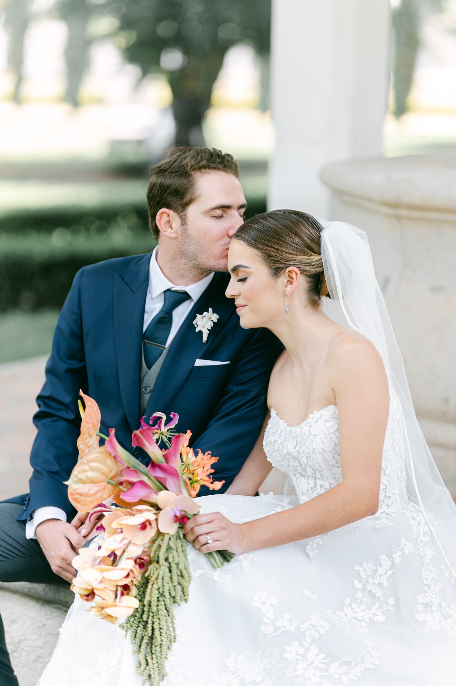 Intimate moment between newlyweds with bride holding colorful bouquet outdoors.