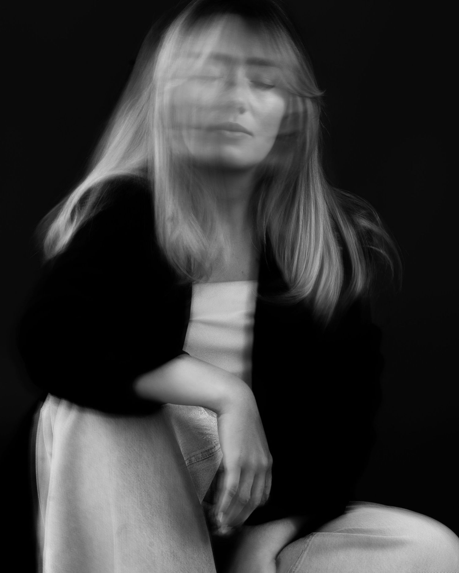 Artistic blurred black and white portrait of a blonde woman with eyes closed in dark setting.