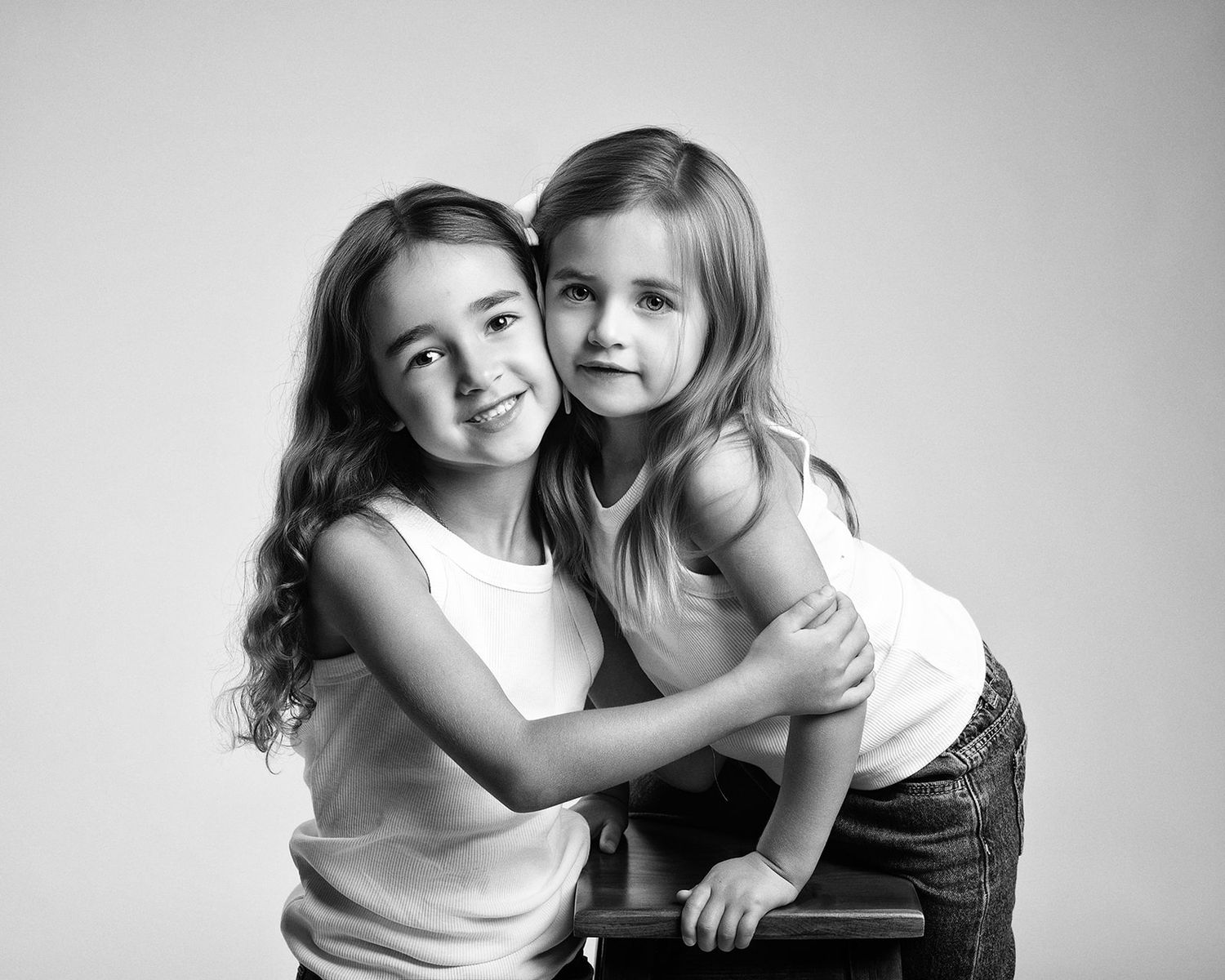 Two young sisters pose together in matching white tank tops in a sweet black and white studio portrait.