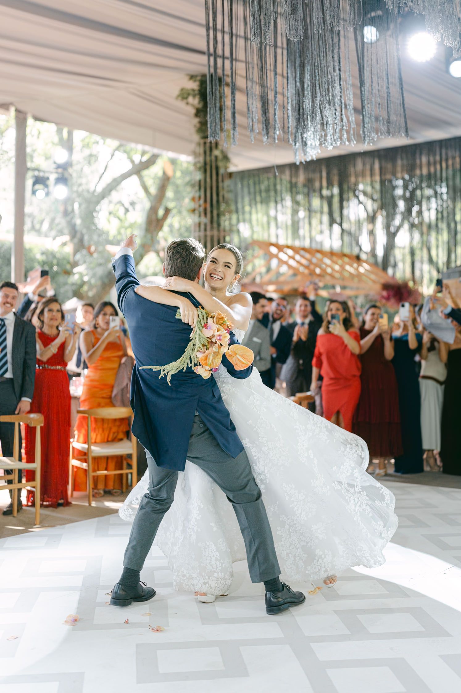 A couple performs their first dance with wedding guests watching under decorative hanging ceiling decor.