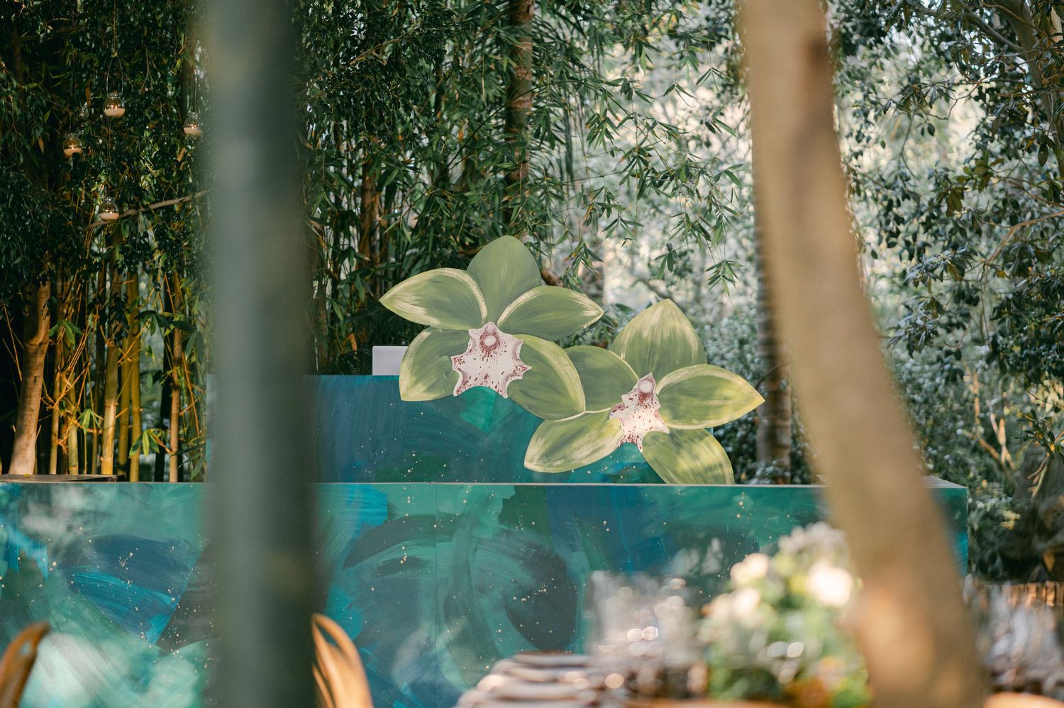 Artistic floral mural with painted orchids displayed outdoors among bamboo trees at a wedding venue.