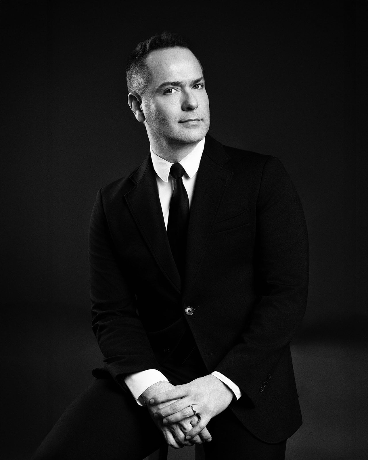 Elegant black and white portrait of a man in a suit seated and looking thoughtfully to the side.