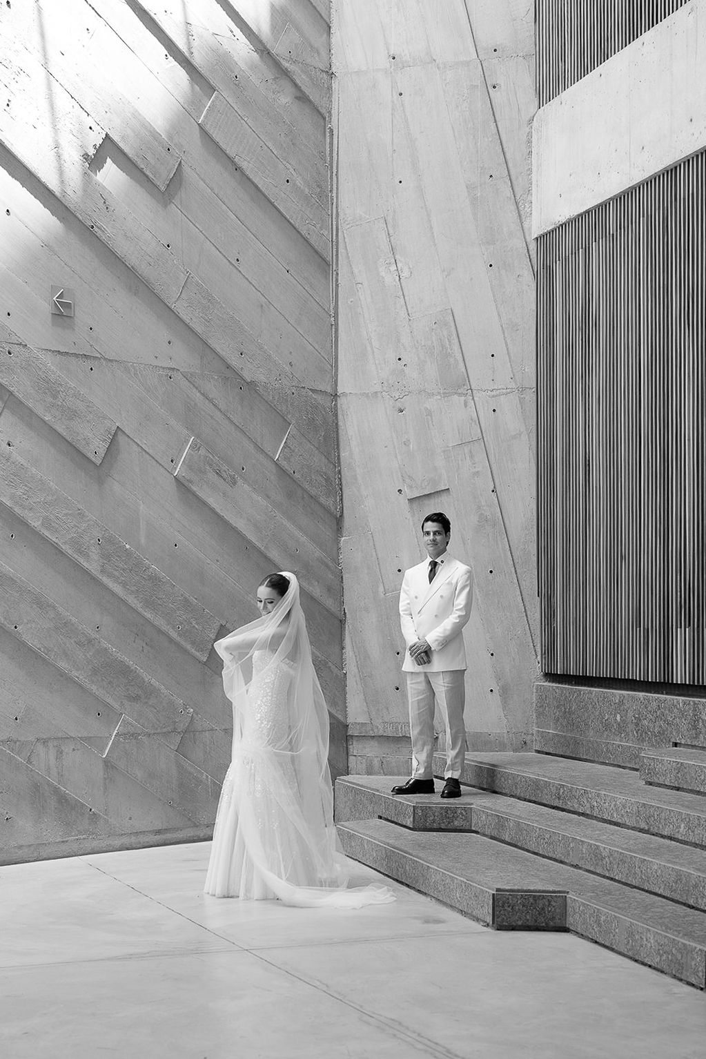 Black and white wedding photo of bride and groom in a modern architectural space.