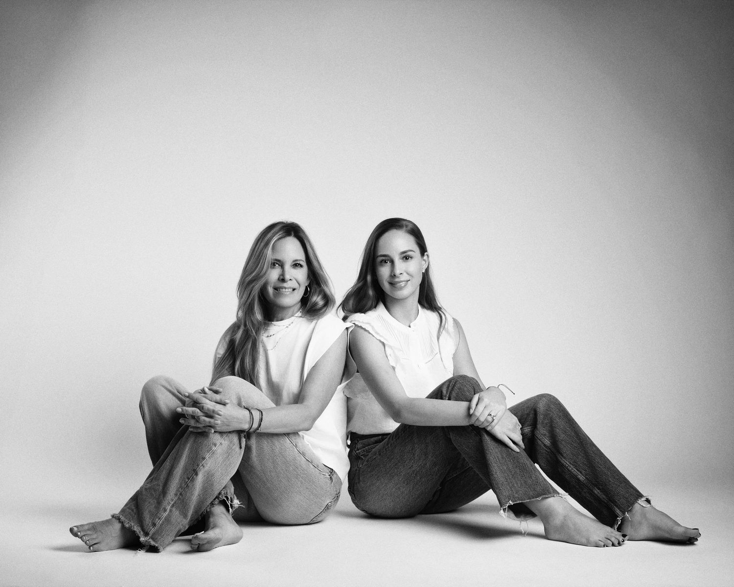Two women sit back-to-back on the floor in a classic black and white studio portrait.