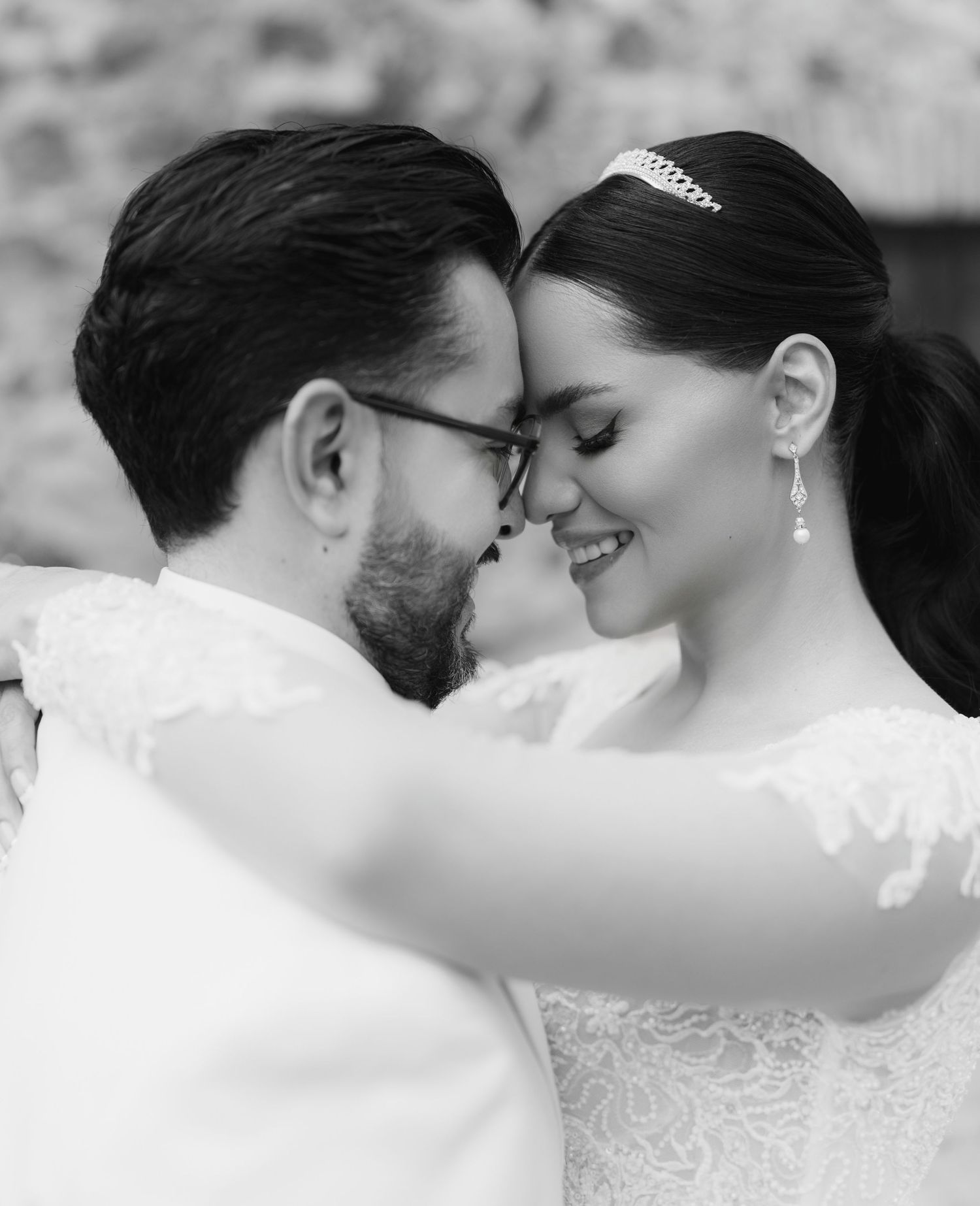 Black and white photo of a couple in wedding attire touching foreheads and smiling at each other.