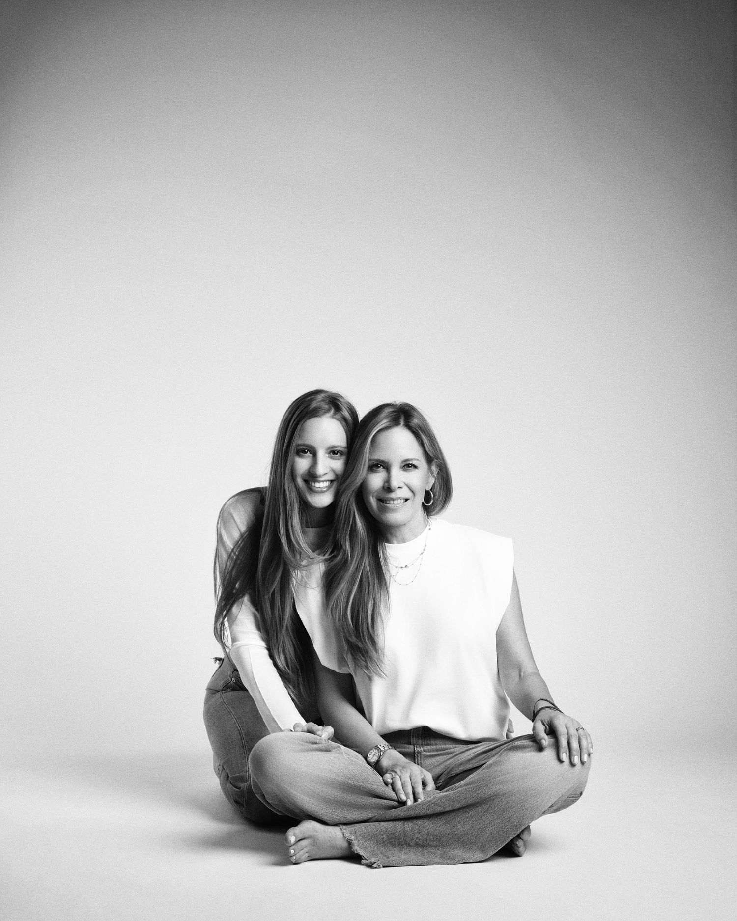 Black and white portrait of two women sitting close together on the floor in a photography studio.