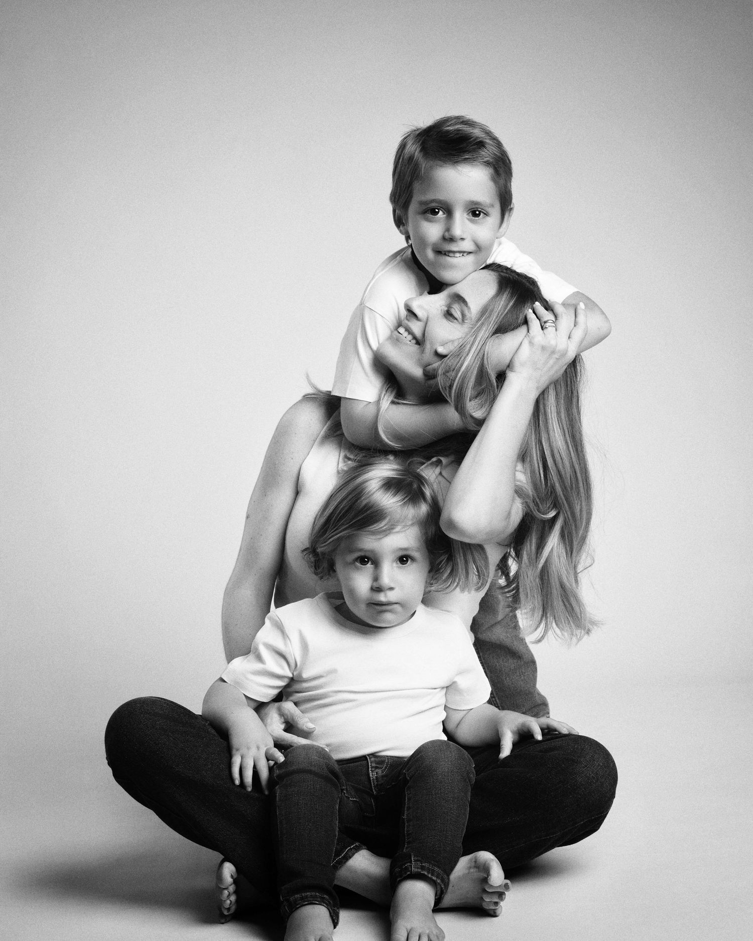 Black and white studio portrait of a mother lying on the floor with her two young children stacked.