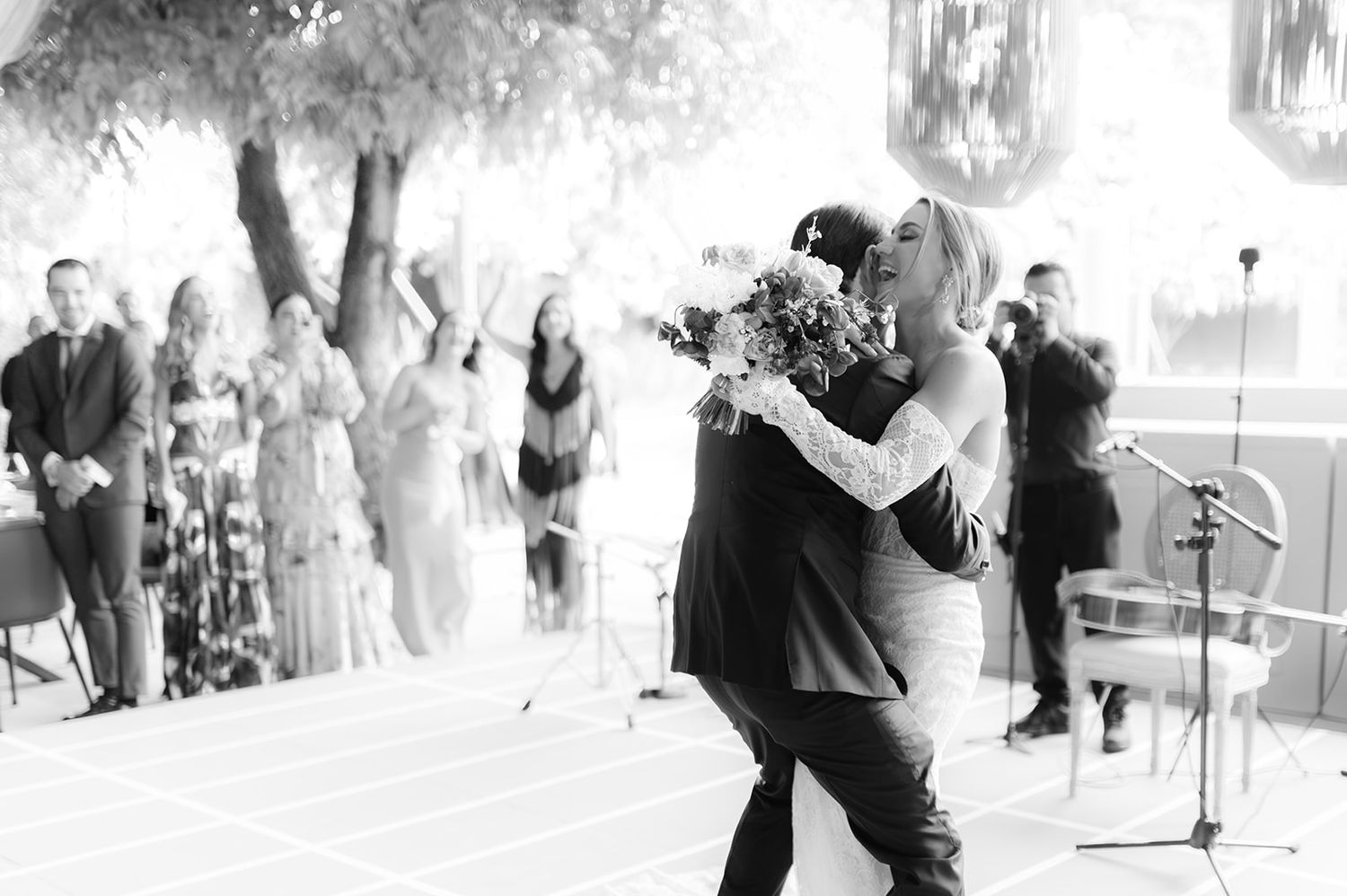 Black and white photo of groom lifting bride in joyful embrace on outdoor wedding dance floor.