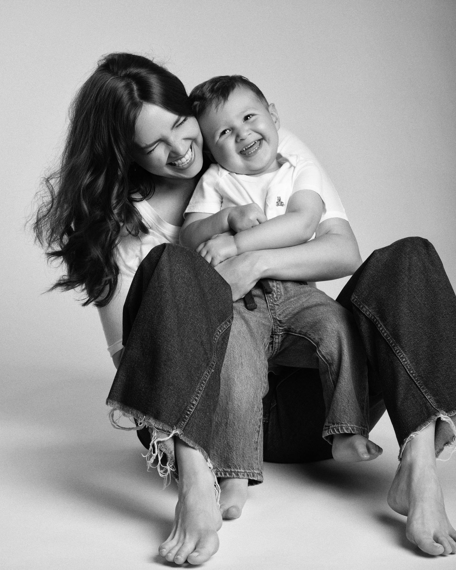 Black and white portrait of a smiling mother holding her laughing baby boy on her lap.