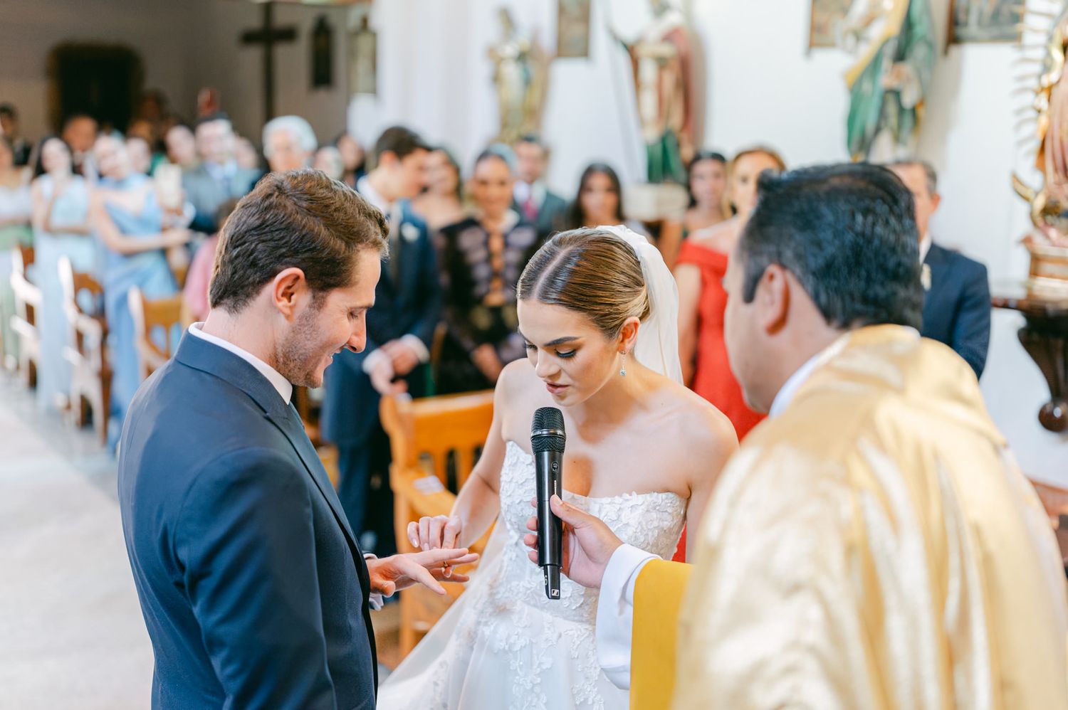 Wedding ceremony taking place in elegant church with cross visible in background and guests seated in pews.
