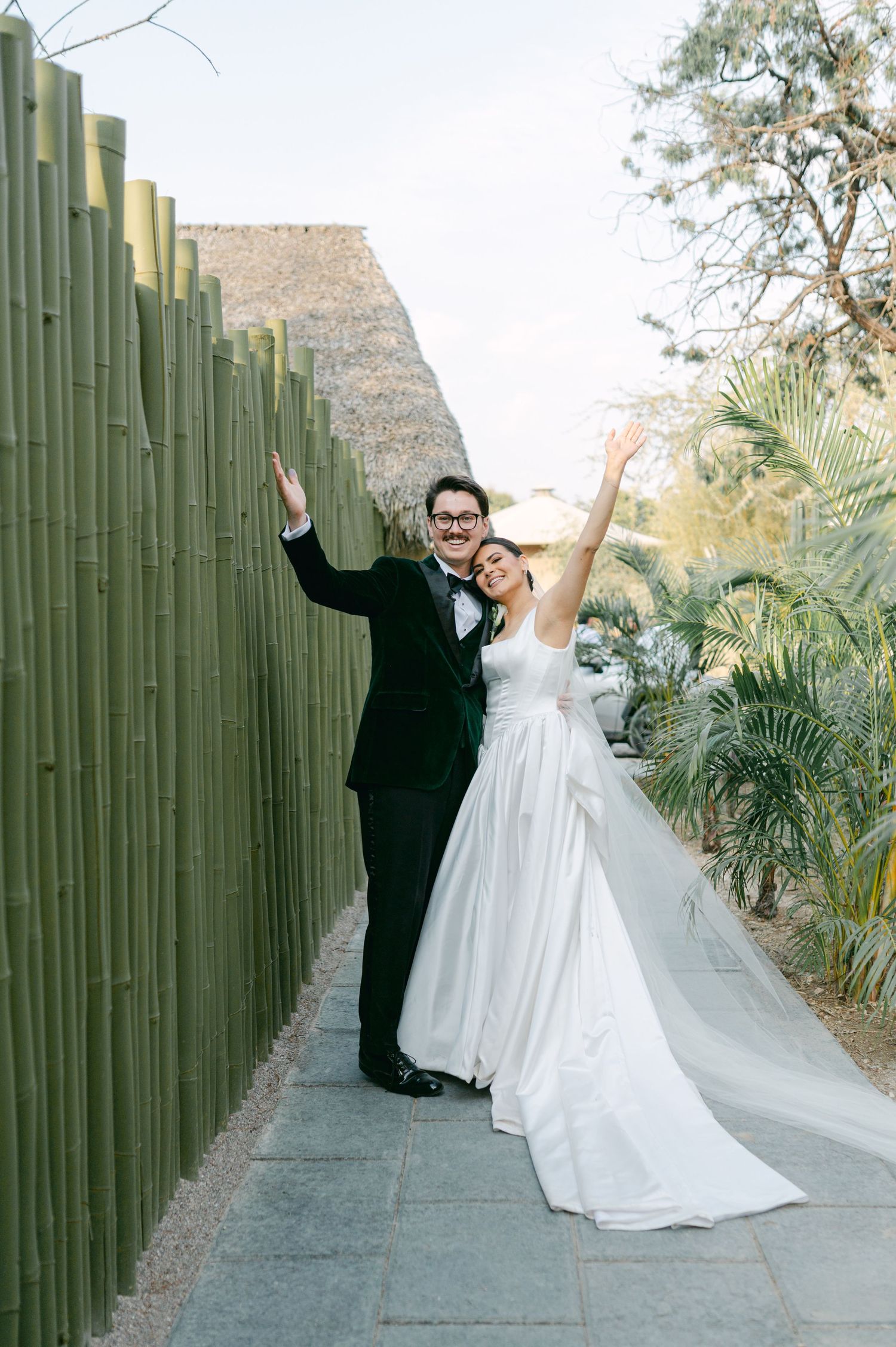 Joyful bride and groom celebrating beside a tall bamboo wall in a tropical wedding setting.