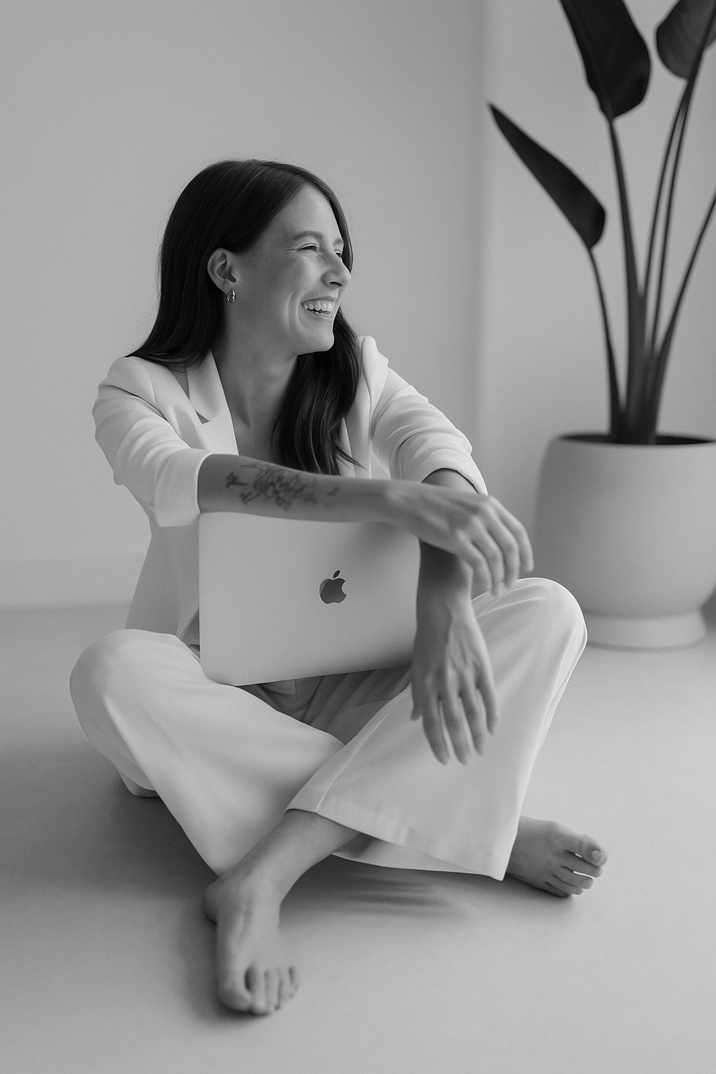 Smiling brunette woman sitting cross-legged on floor holding Apple MacBook laptop.