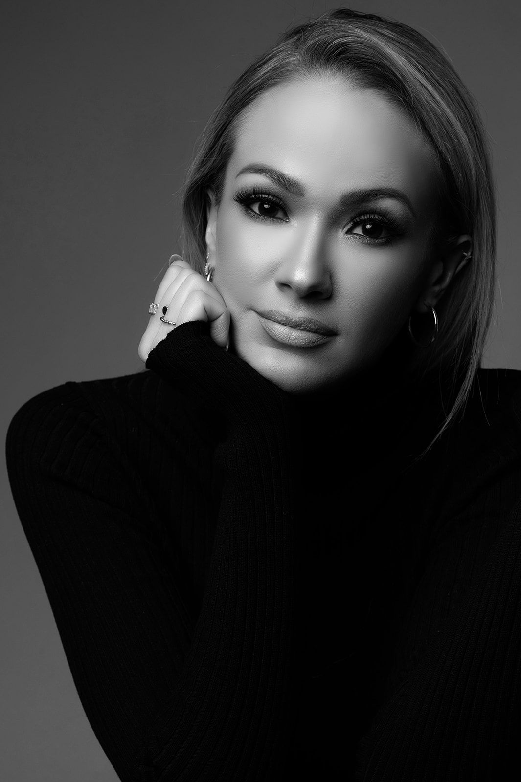 Black and white close-up portrait of a blonde woman in a black turtleneck with elegant jewelry.