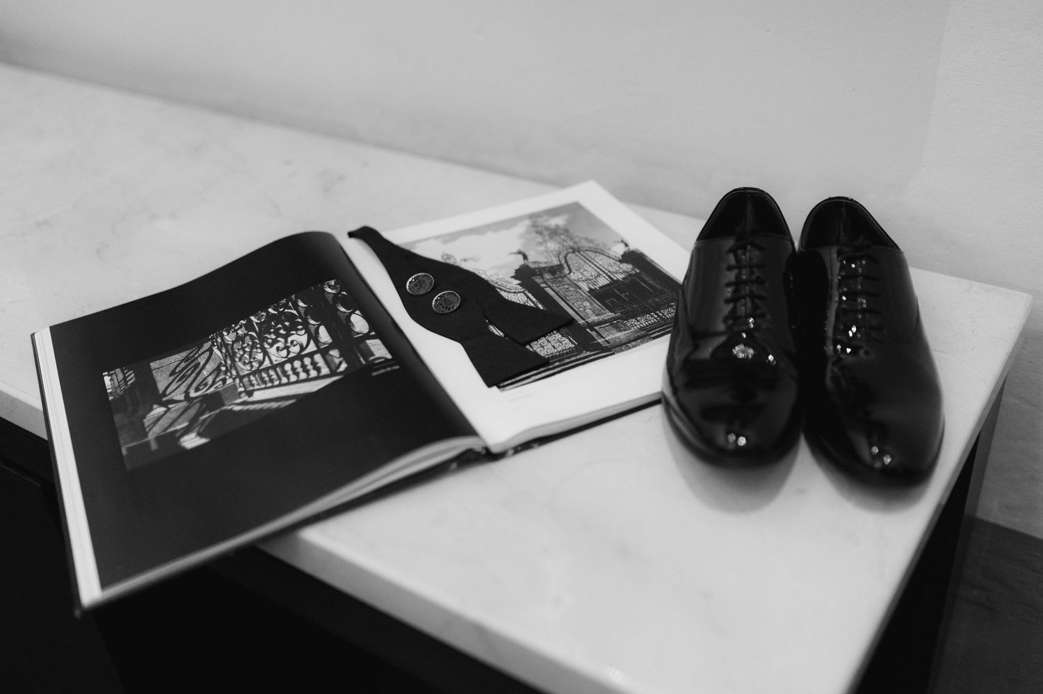 Black and white photo of patent leather dress shoes and open book on marble surface.