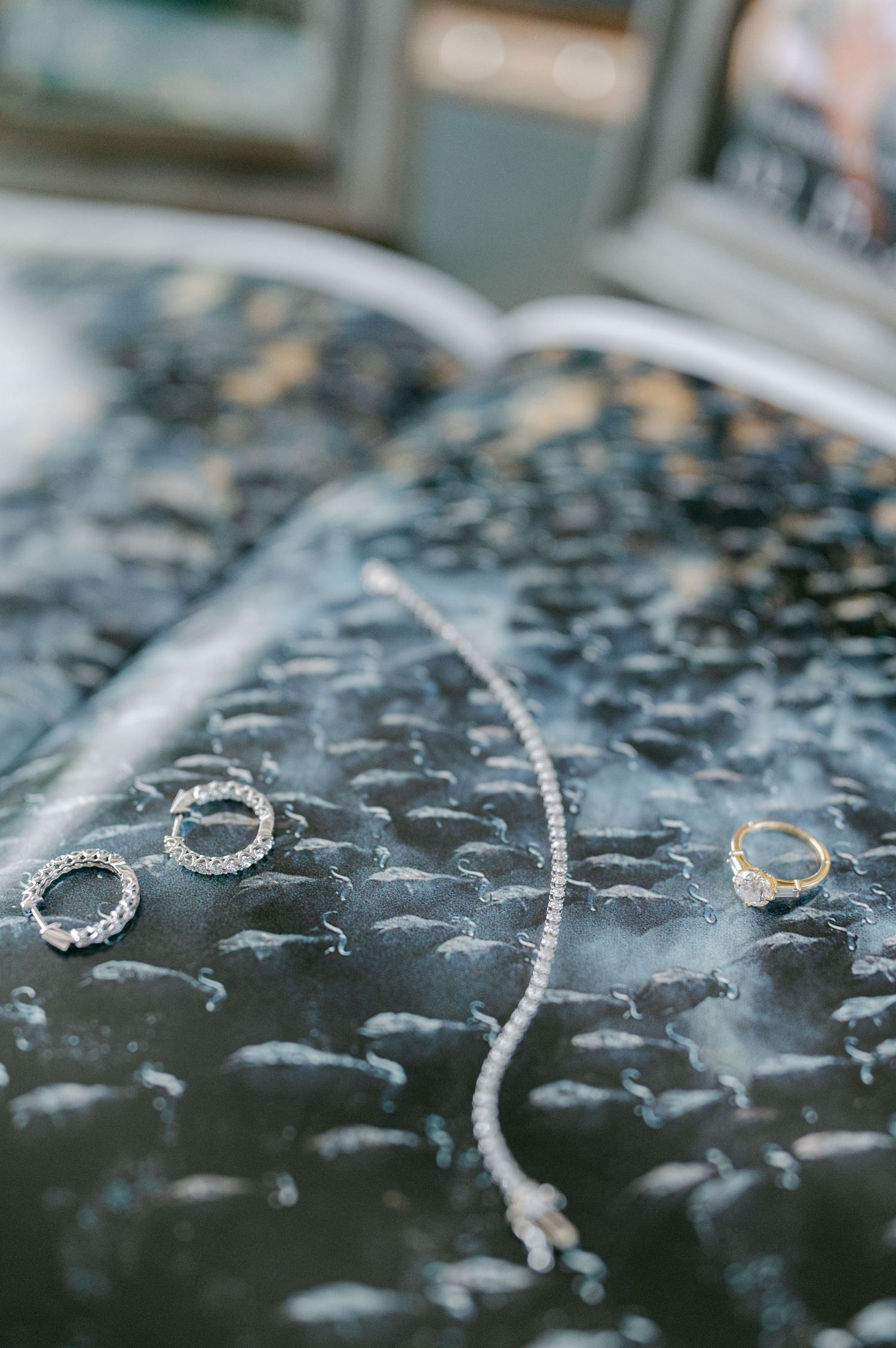 Wedding jewelry flat lay featuring diamond rings and a delicate bracelet on dark textured surface.