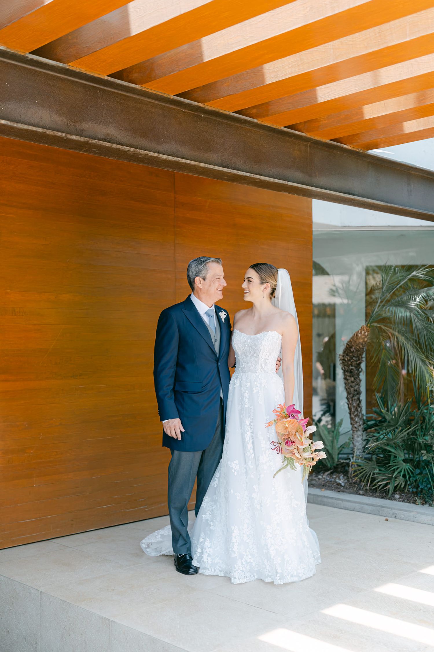 Bride in lace gown with veil sharing a loving glance with father before walking down aisle.