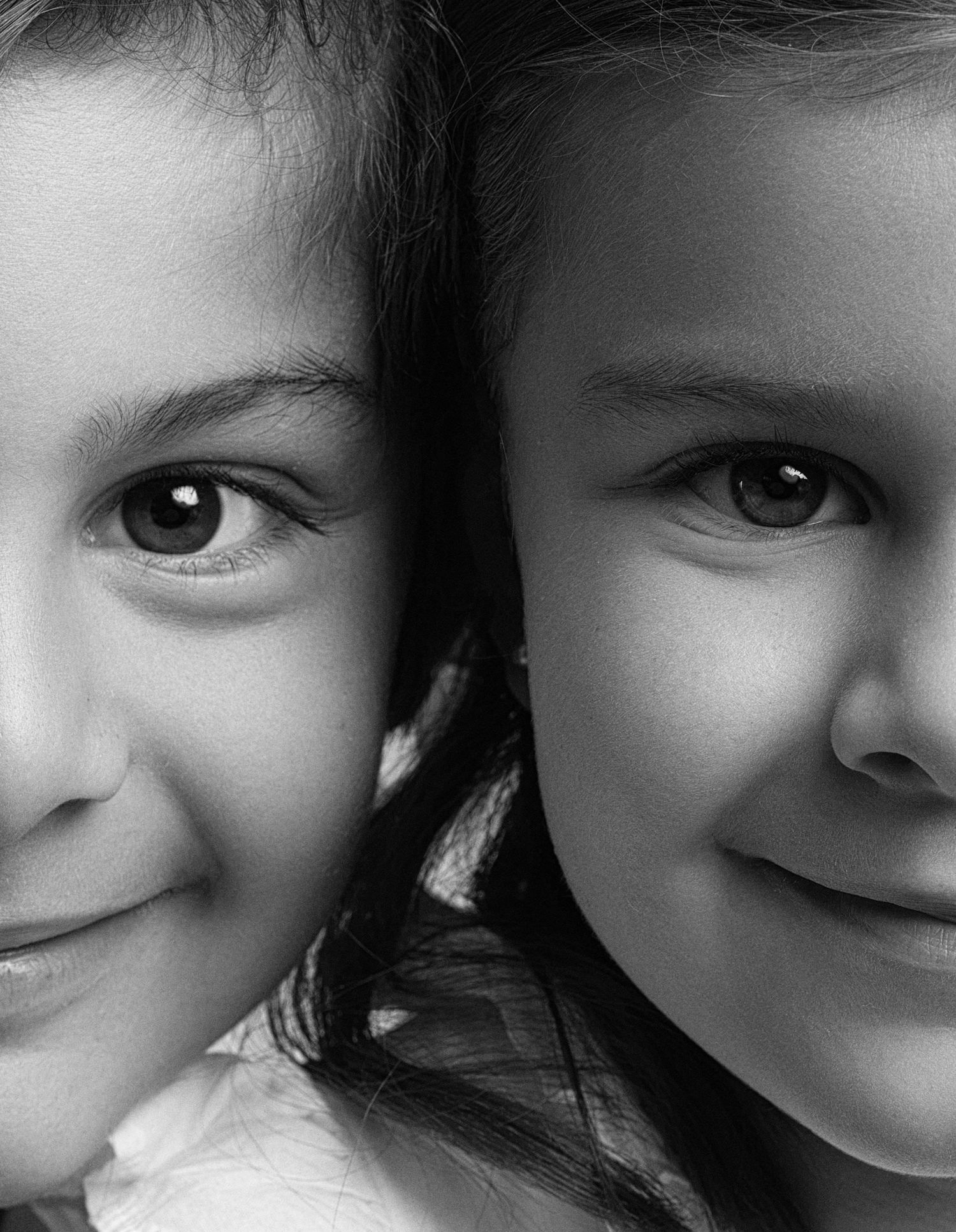 Black and white close-up portrait of two young girls smiling warmly cheek to cheek.